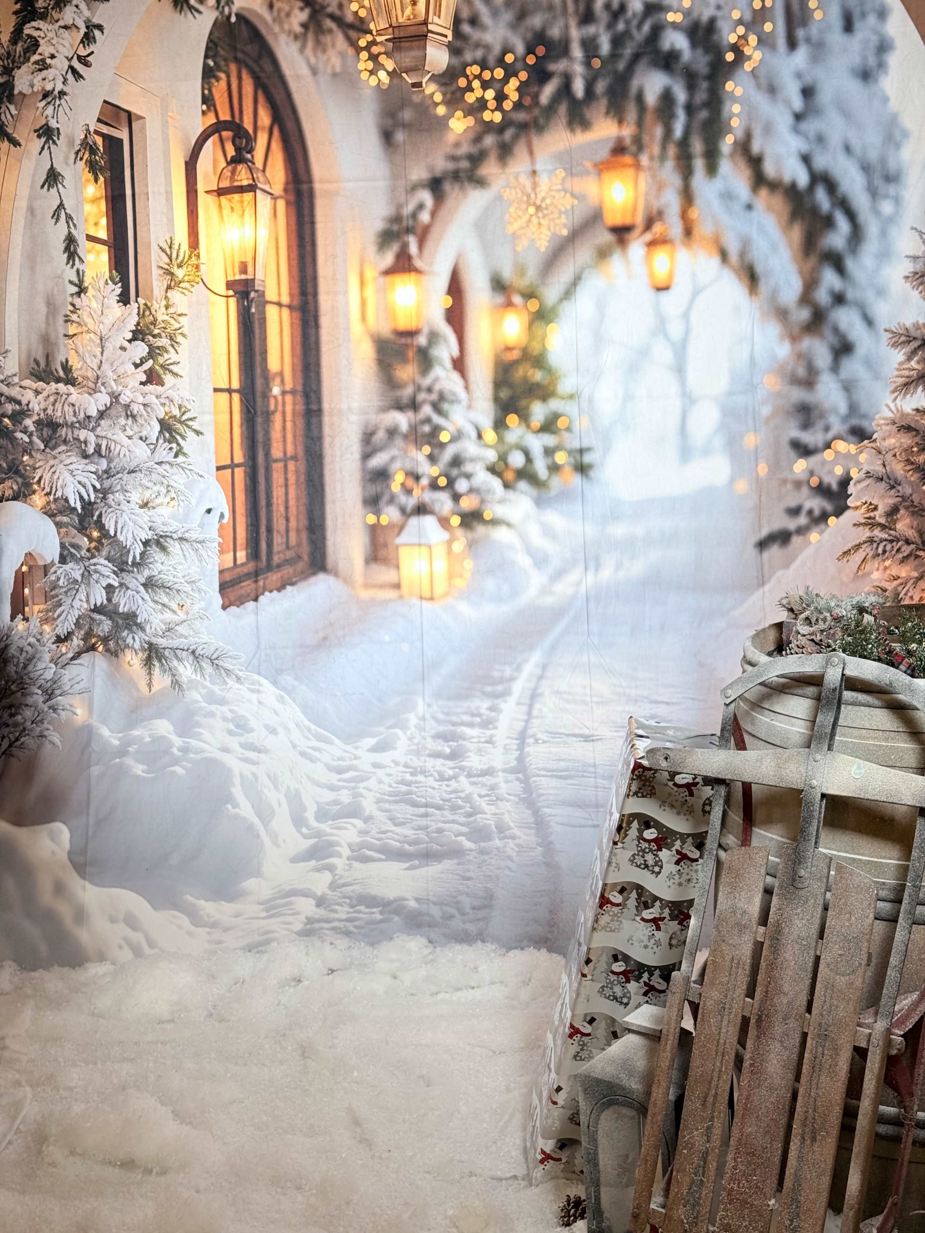 The scene features a winter-themed backdrop with snow-covered paths, decorated trees, and warm lanterns, alongside a wooden sled and wrapped gifts in the foreground.