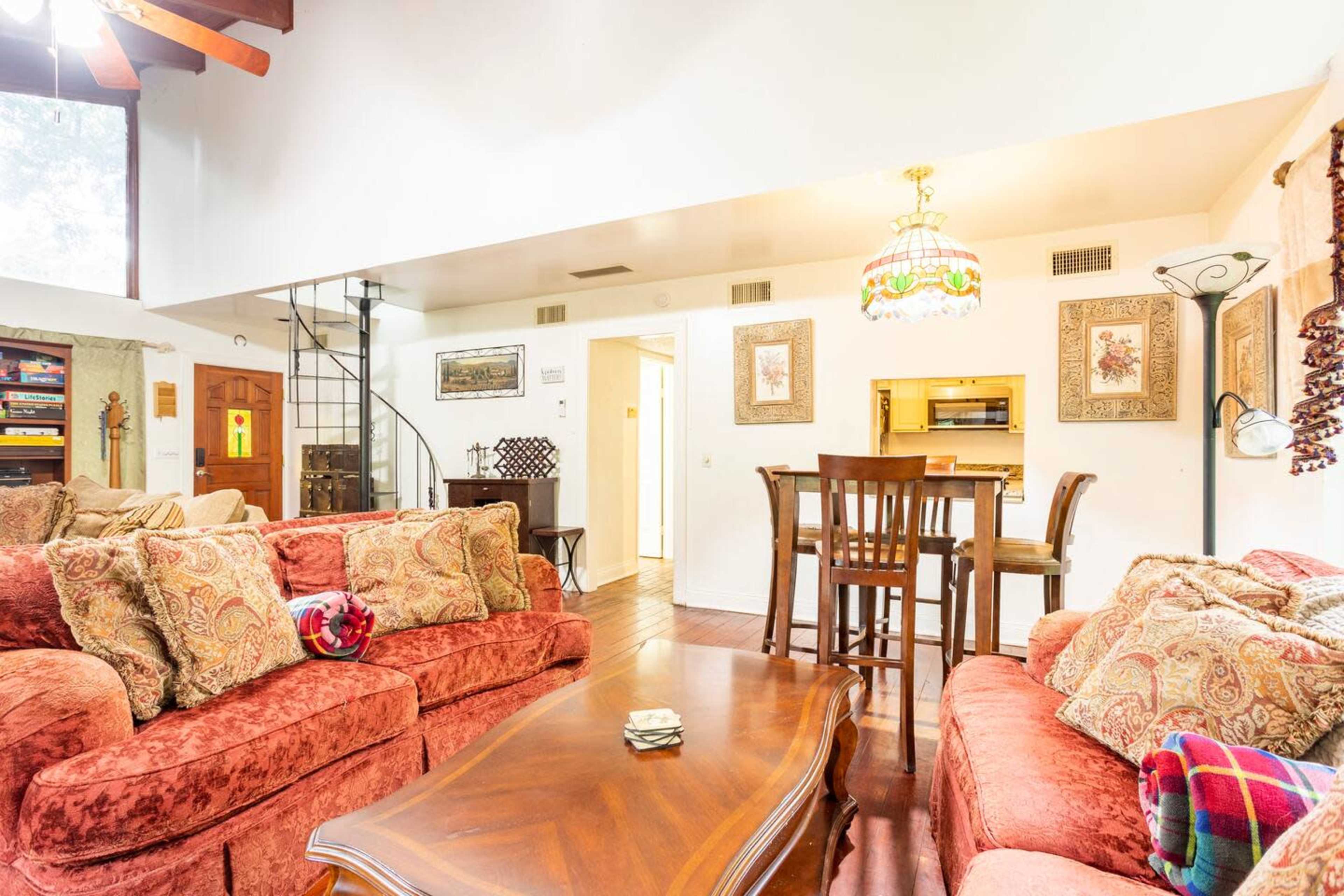 The image shows a living room with red couches, a wooden coffee table, and a dining area visible in the background.