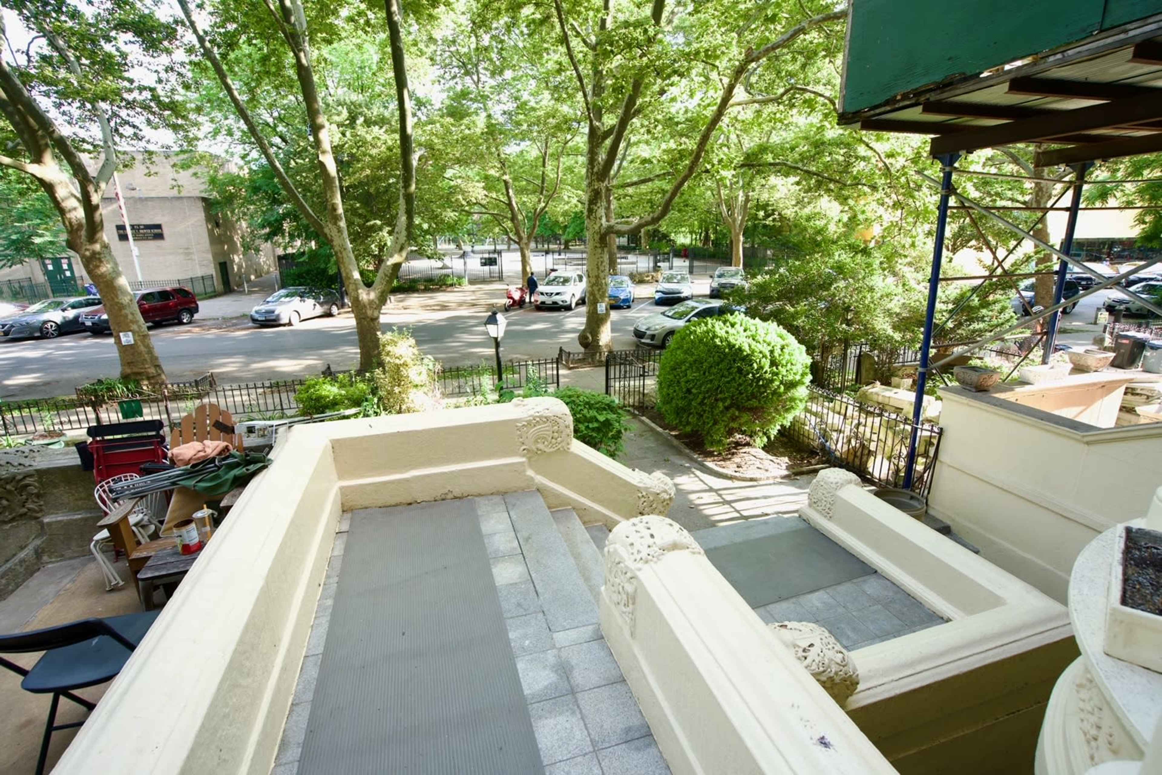 A view from a staircase leading down to a garden area with trees and parked cars visible in the background.