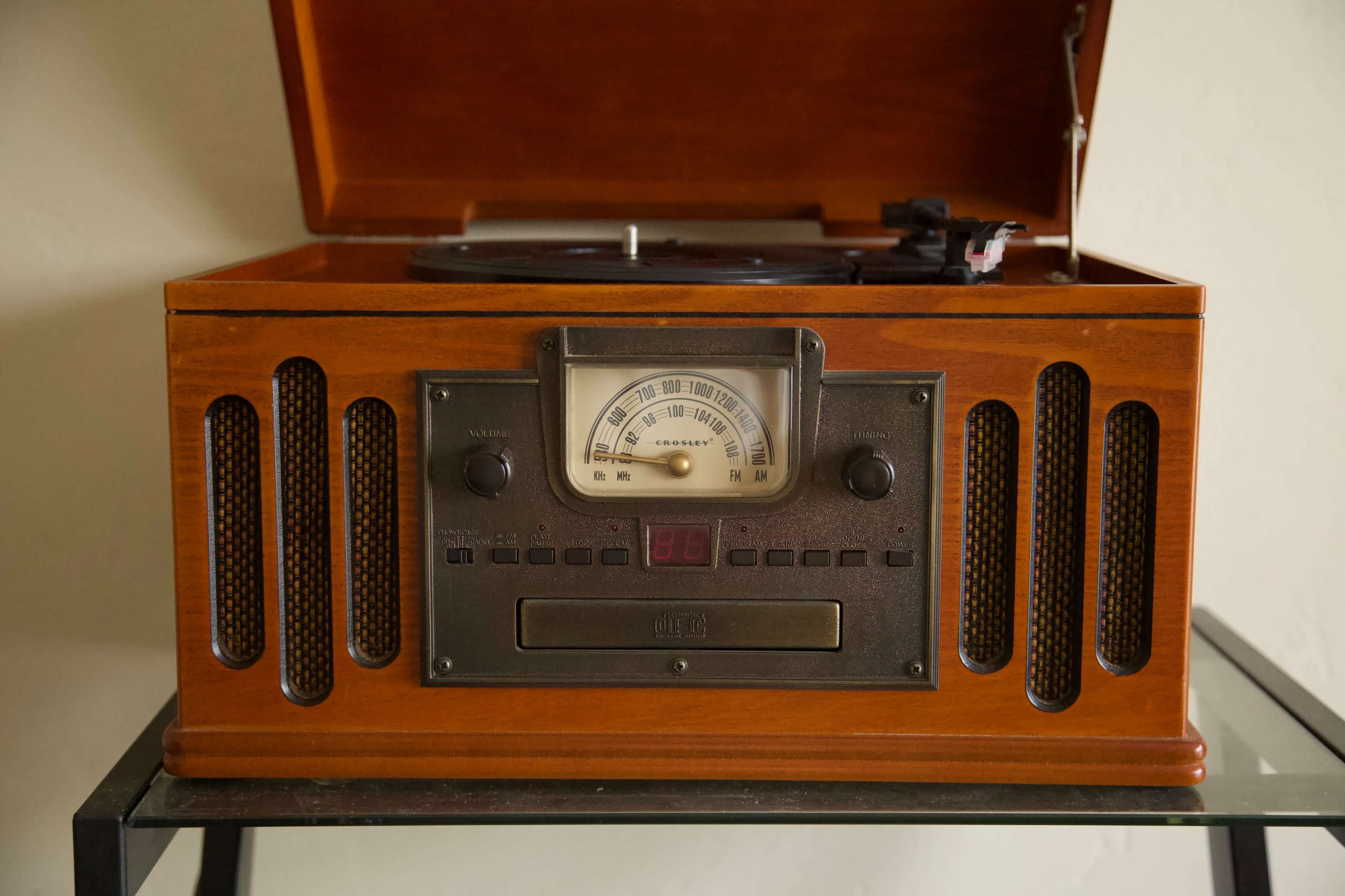 The image shows a vintage wooden record player with a hinged lid, featuring metal knobs and a dial on the front.