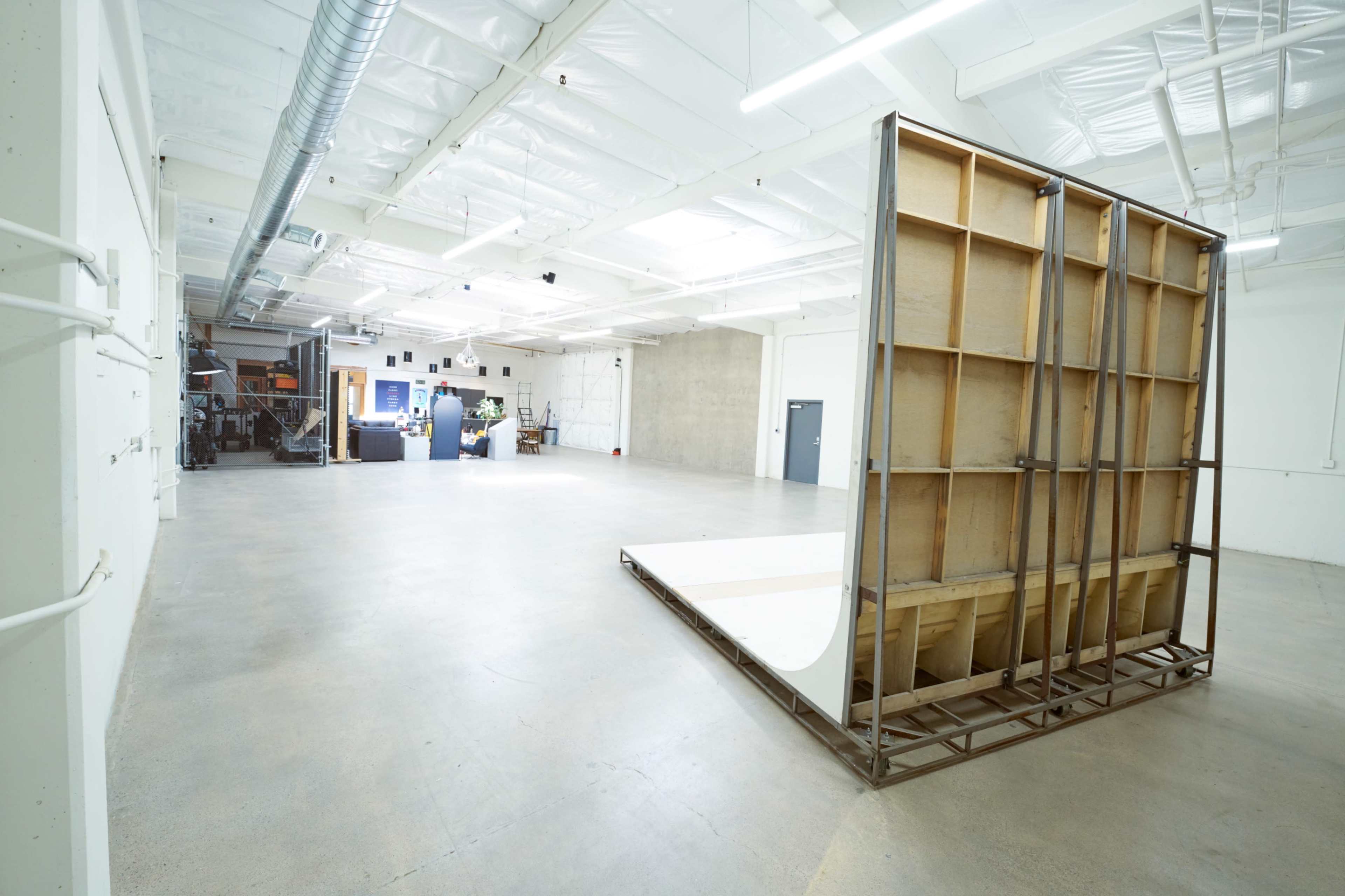 The image shows a spacious, empty industrial room with a large wooden structure set against one wall.