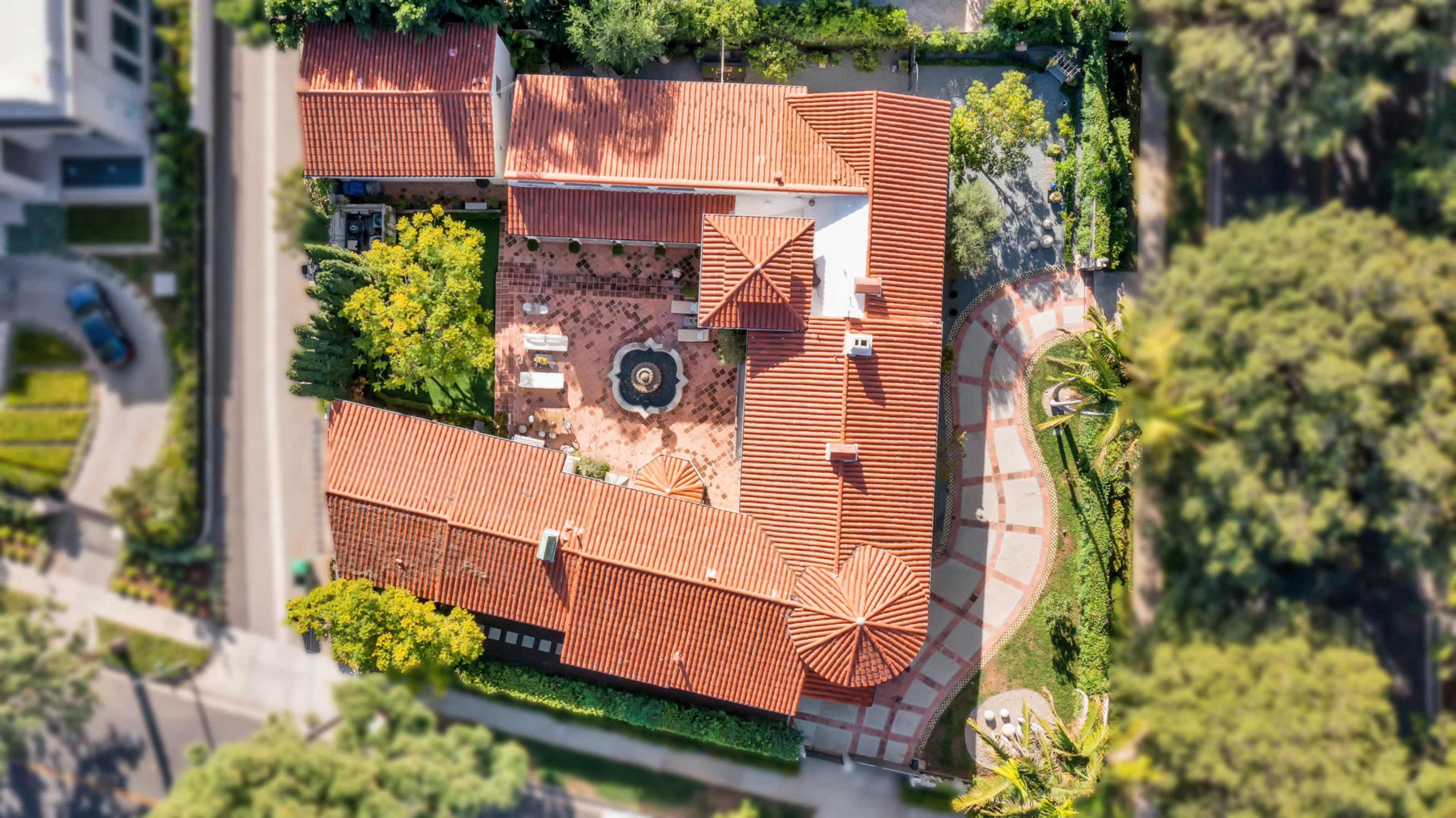 An aerial view of a residential property with a red-tiled roof, surrounded by trees and a landscaped yard.
