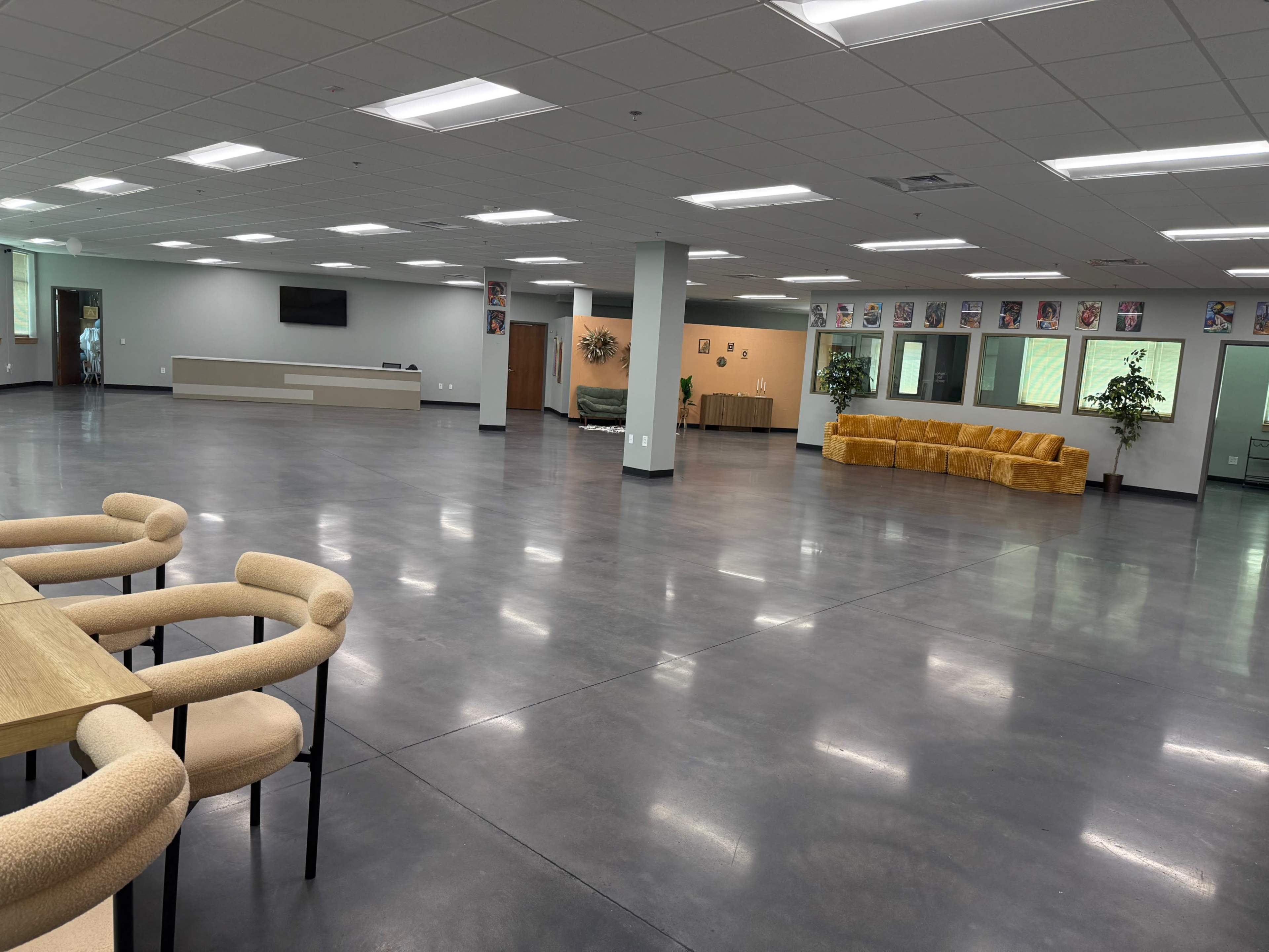 The image shows a spacious, modern room with polished concrete floors, several seating areas, and office-like spaces along the walls.