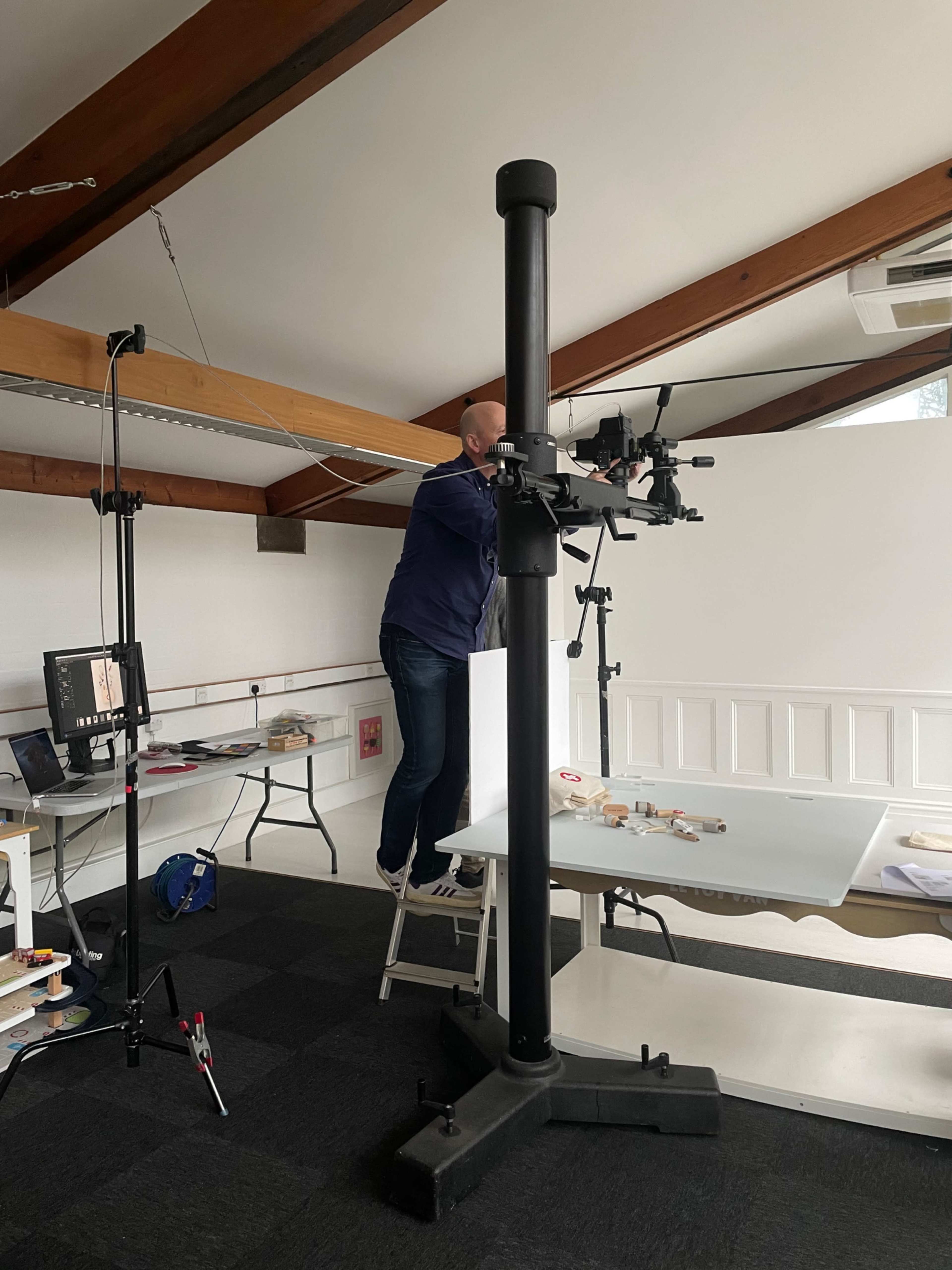 A person is adjusting a camera mounted on a tall tripod in a bright, open studio space.