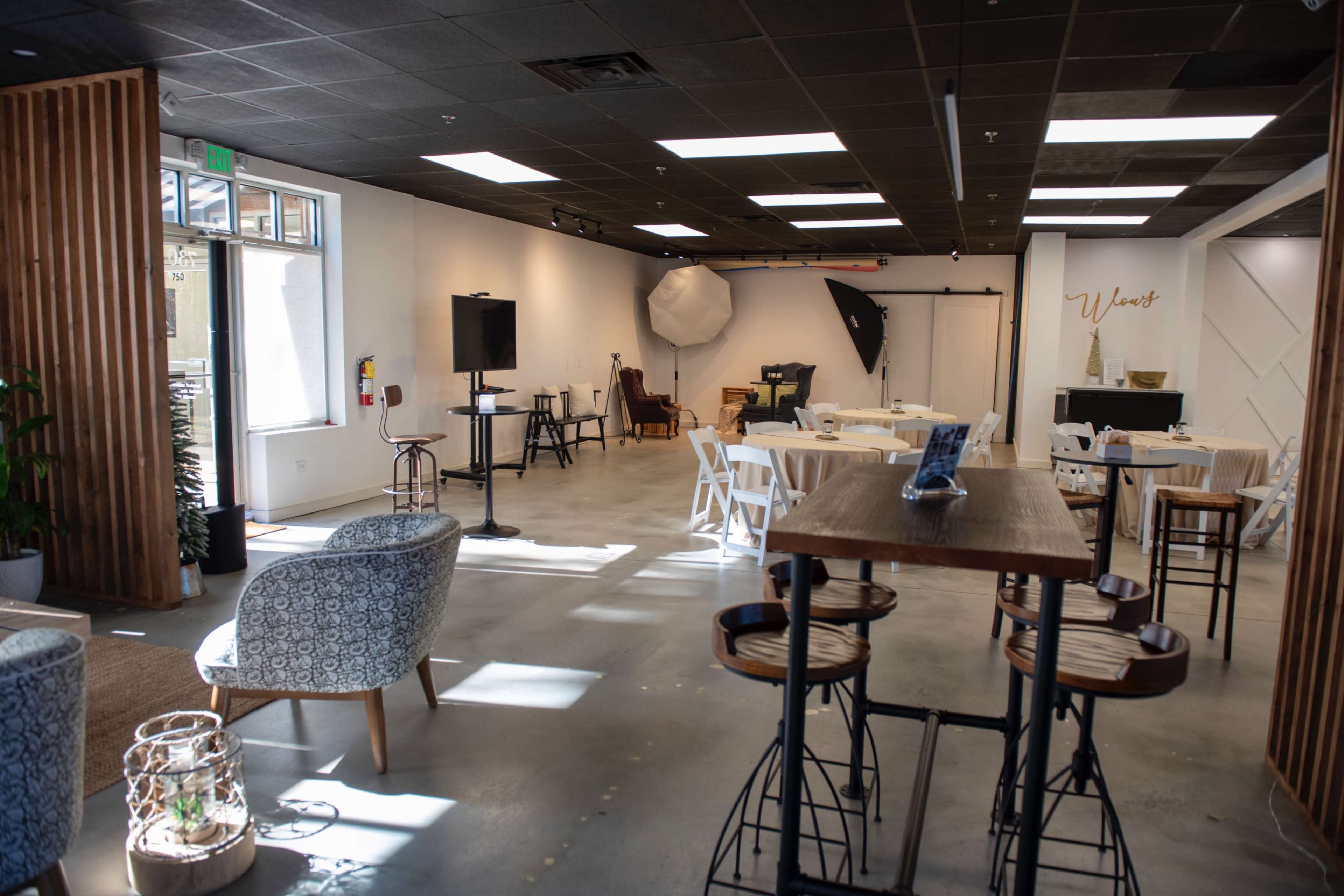 The image shows a spacious, modern event space with a mix of tables and chairs, equipment for photography, and bright lighting.