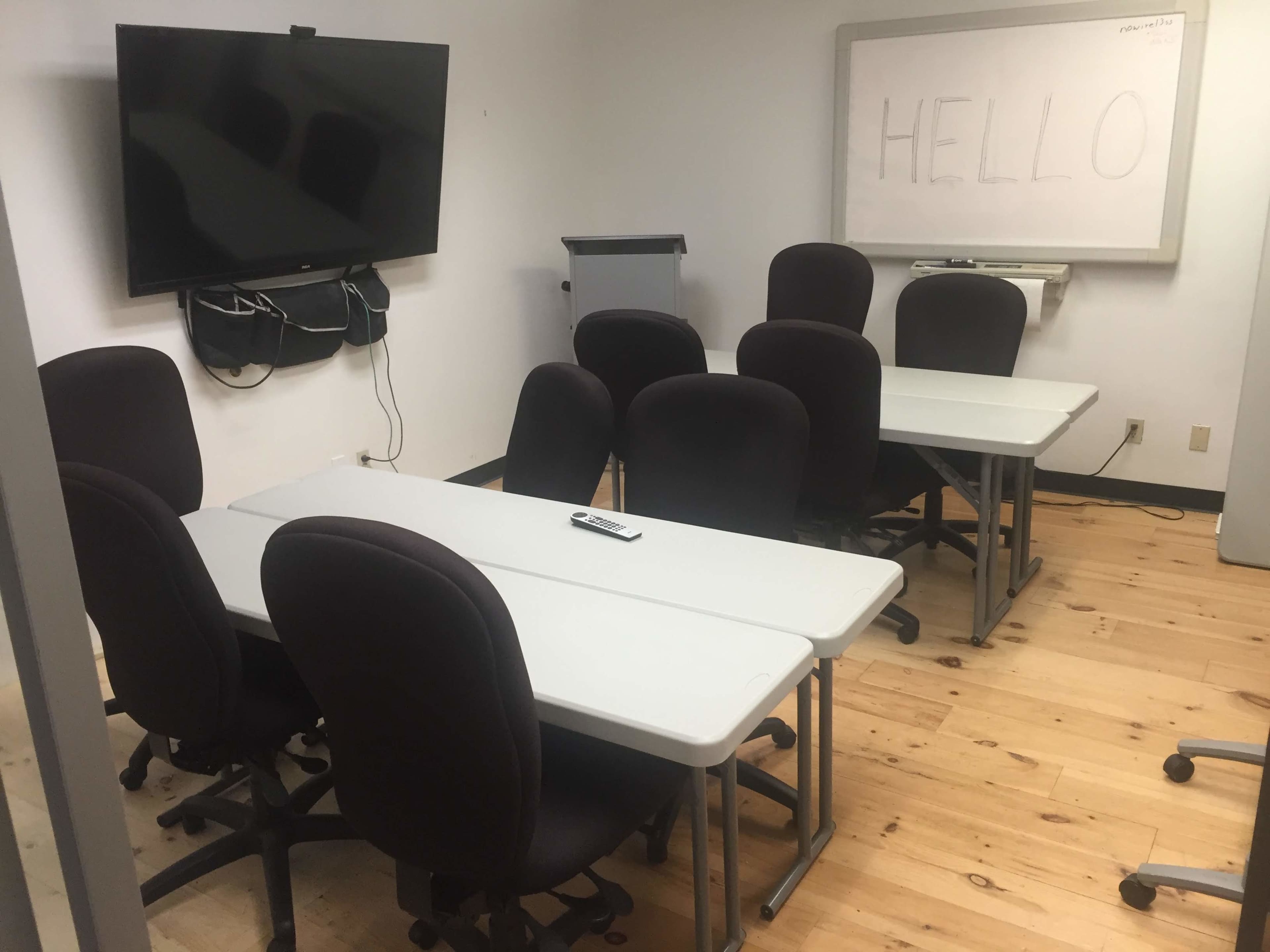 A conference room features several tables and chairs, a television mounted on the wall, and a whiteboard with the word "HELLO" written on it.
