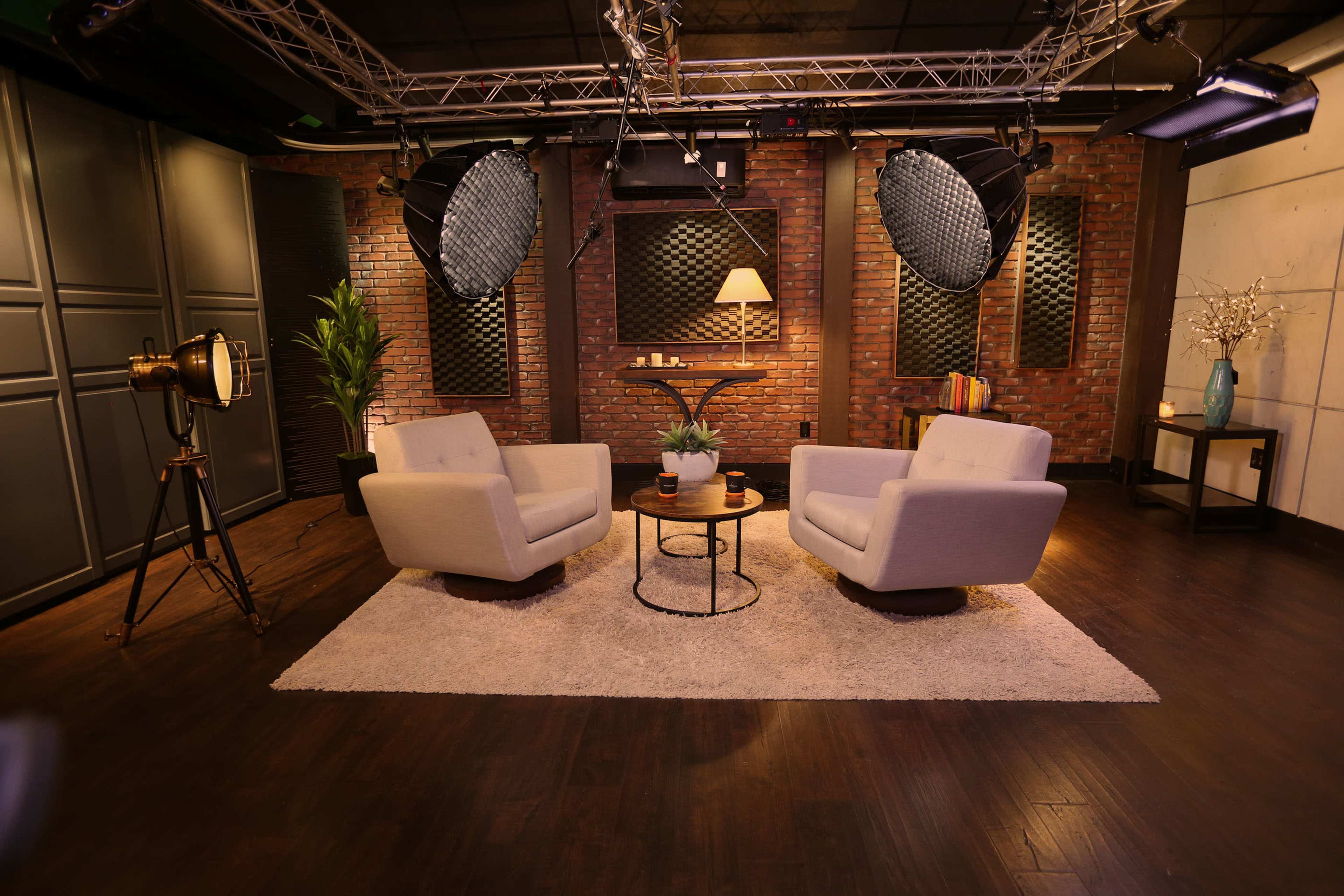 A cozy studio setting features two armchairs facing each other with a small round table in between, surrounded by brick walls and soft lighting.