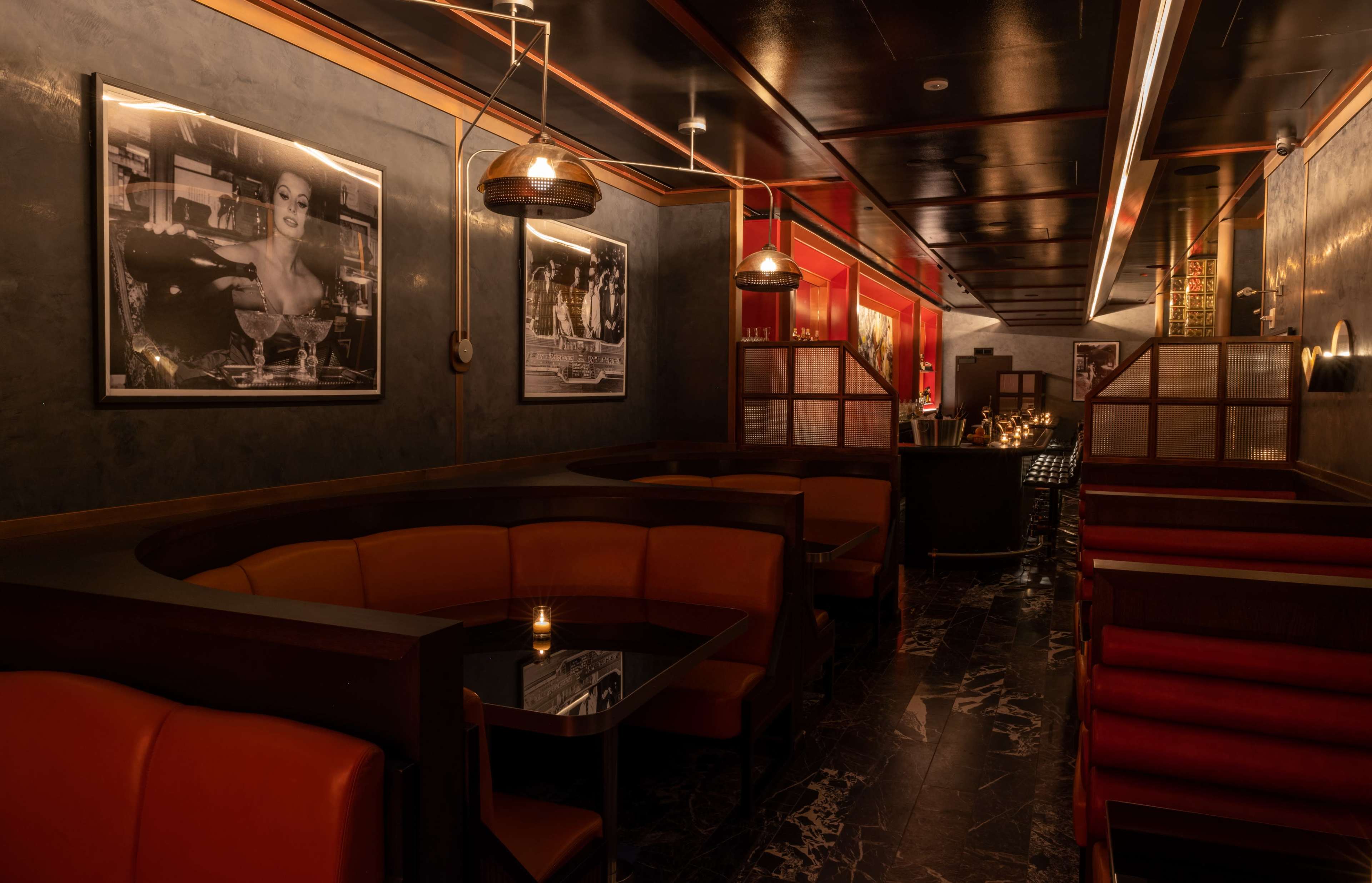 A dimly lit restaurant interior with curved leather seating, marble flooring, and vintage black-and-white photographs on the walls.