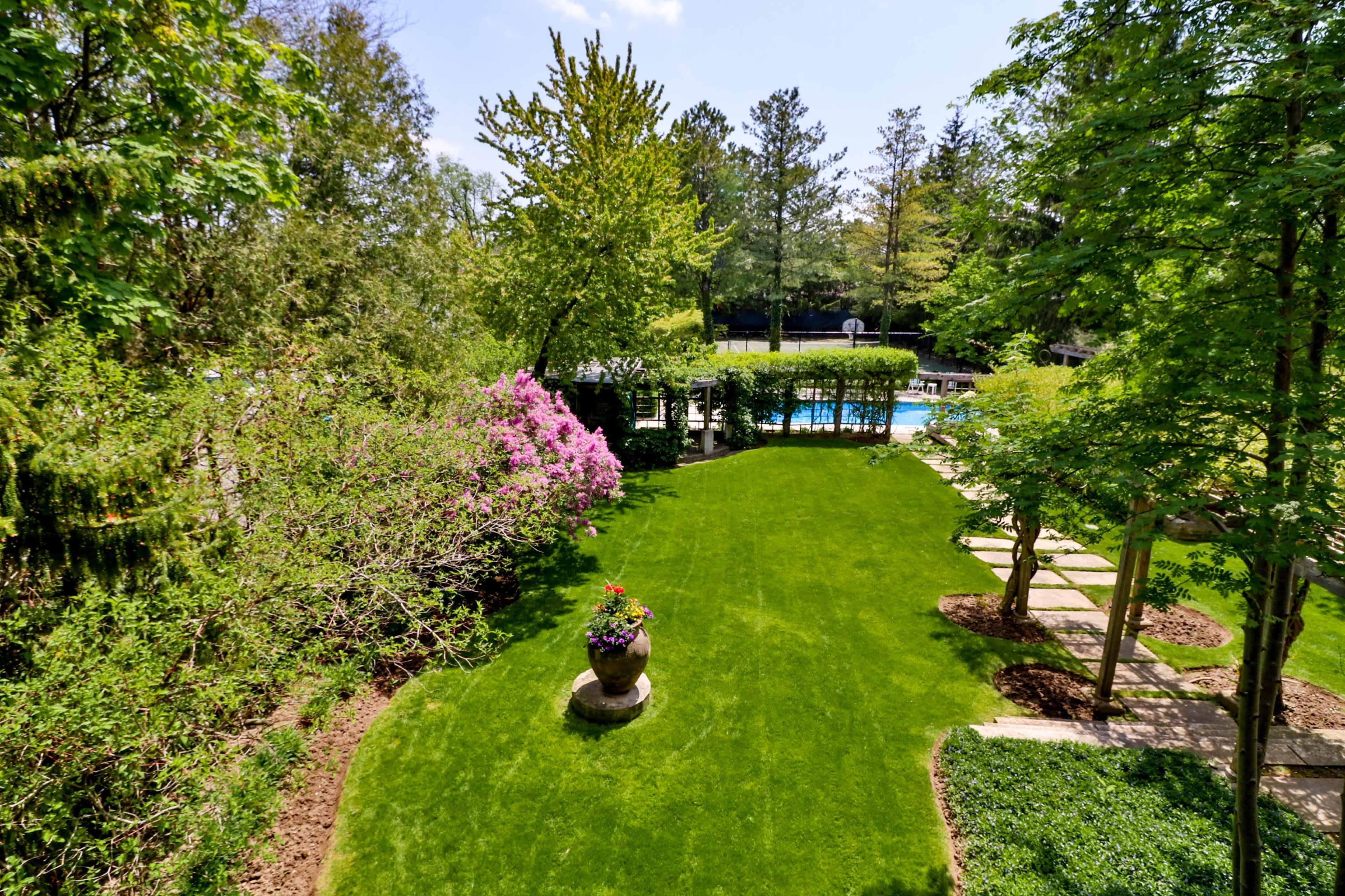 A landscaped garden with vibrant greenery, flowering plants, and a swimming pool in the background.