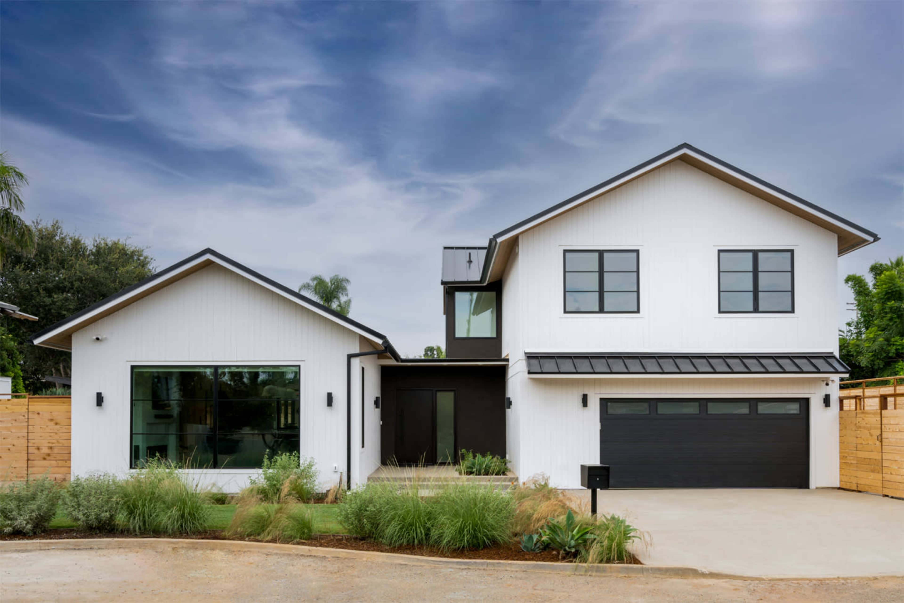 A modern two-story house with a white exterior, black accents, and a large front driveway surrounded by landscaping.