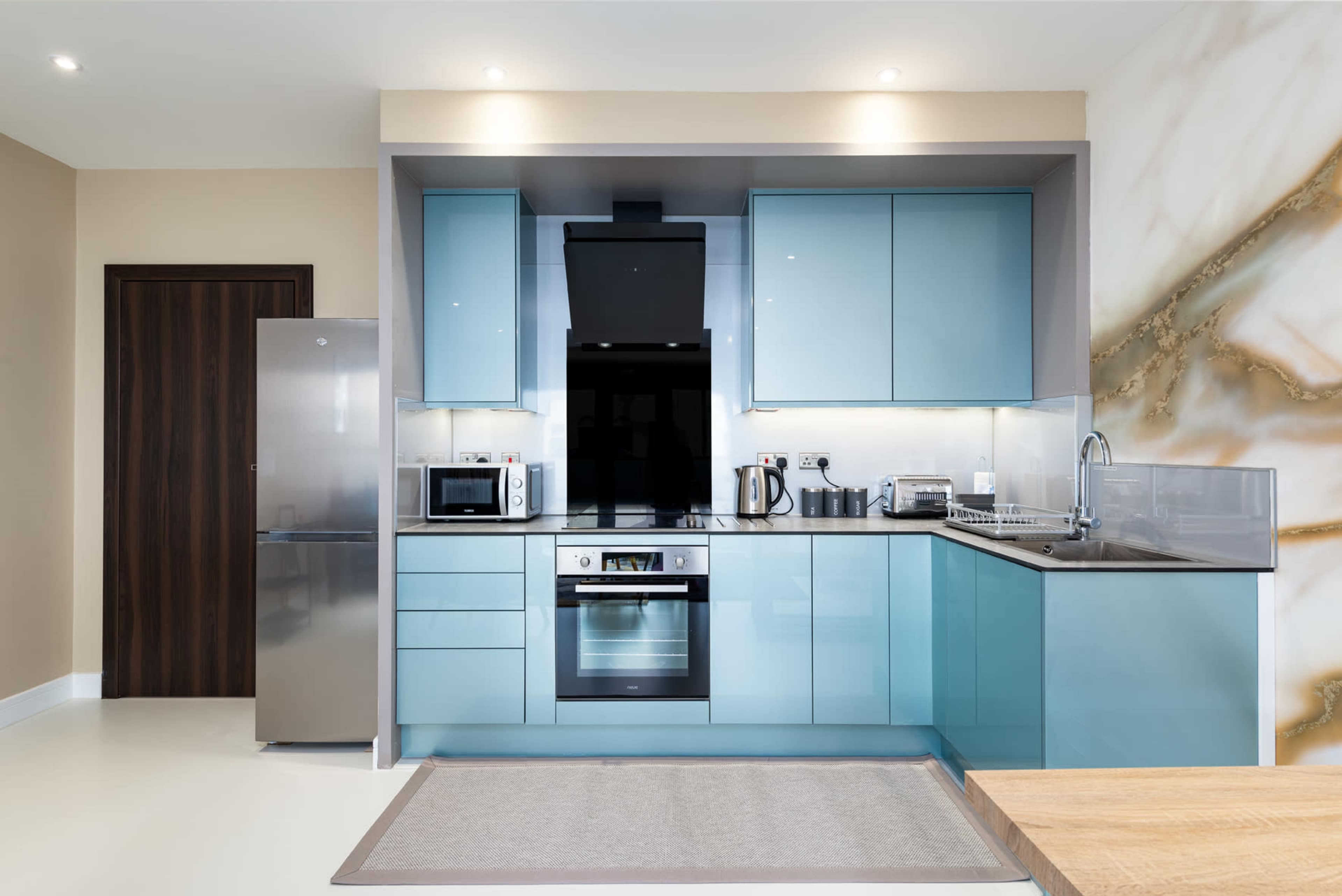 A modern kitchen featuring turquoise cabinets, stainless steel appliances, and a light-colored countertop.