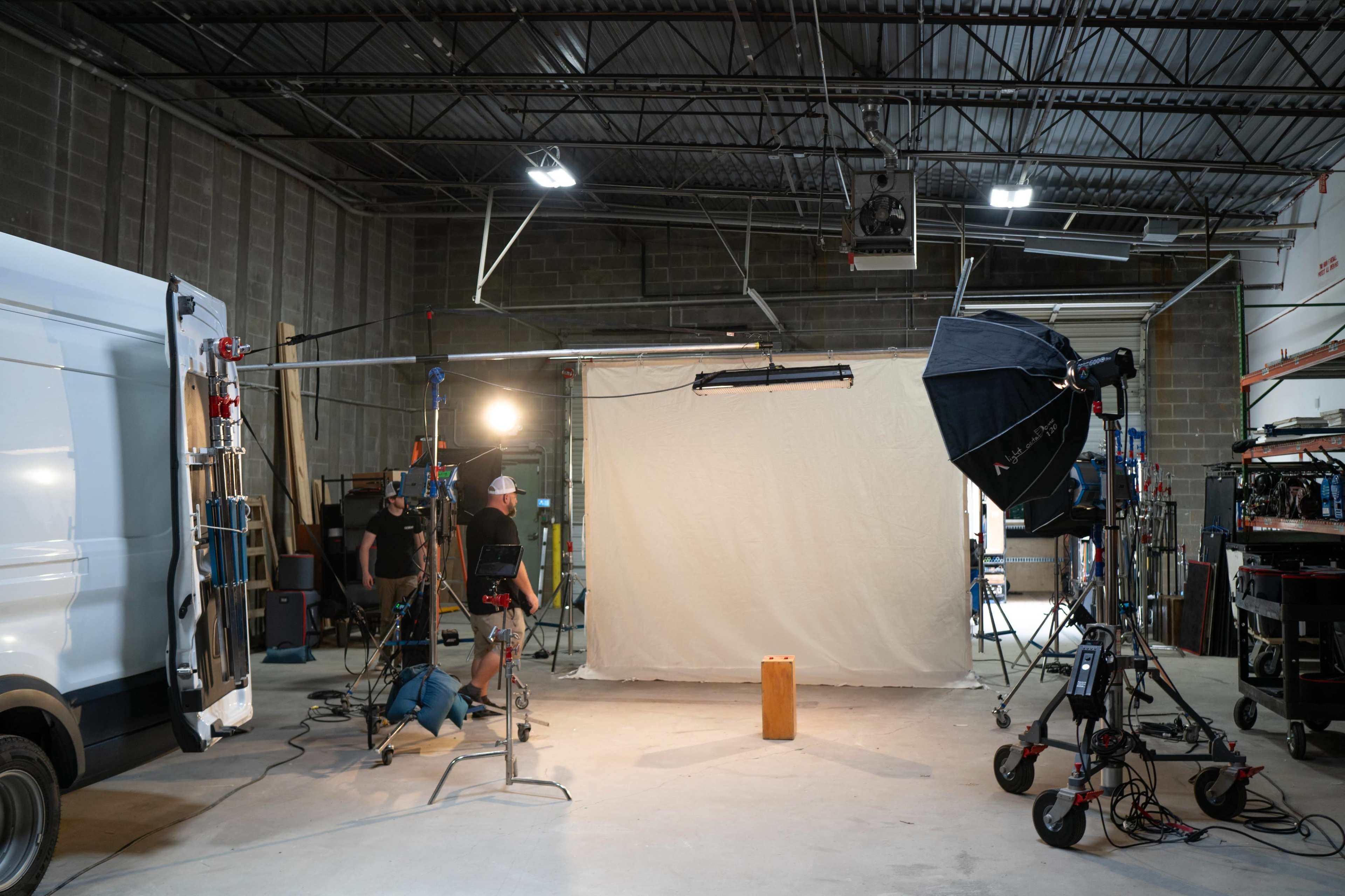 A photography studio setup featuring a backdrop, lighting equipment, and crew members preparing for a shoot.