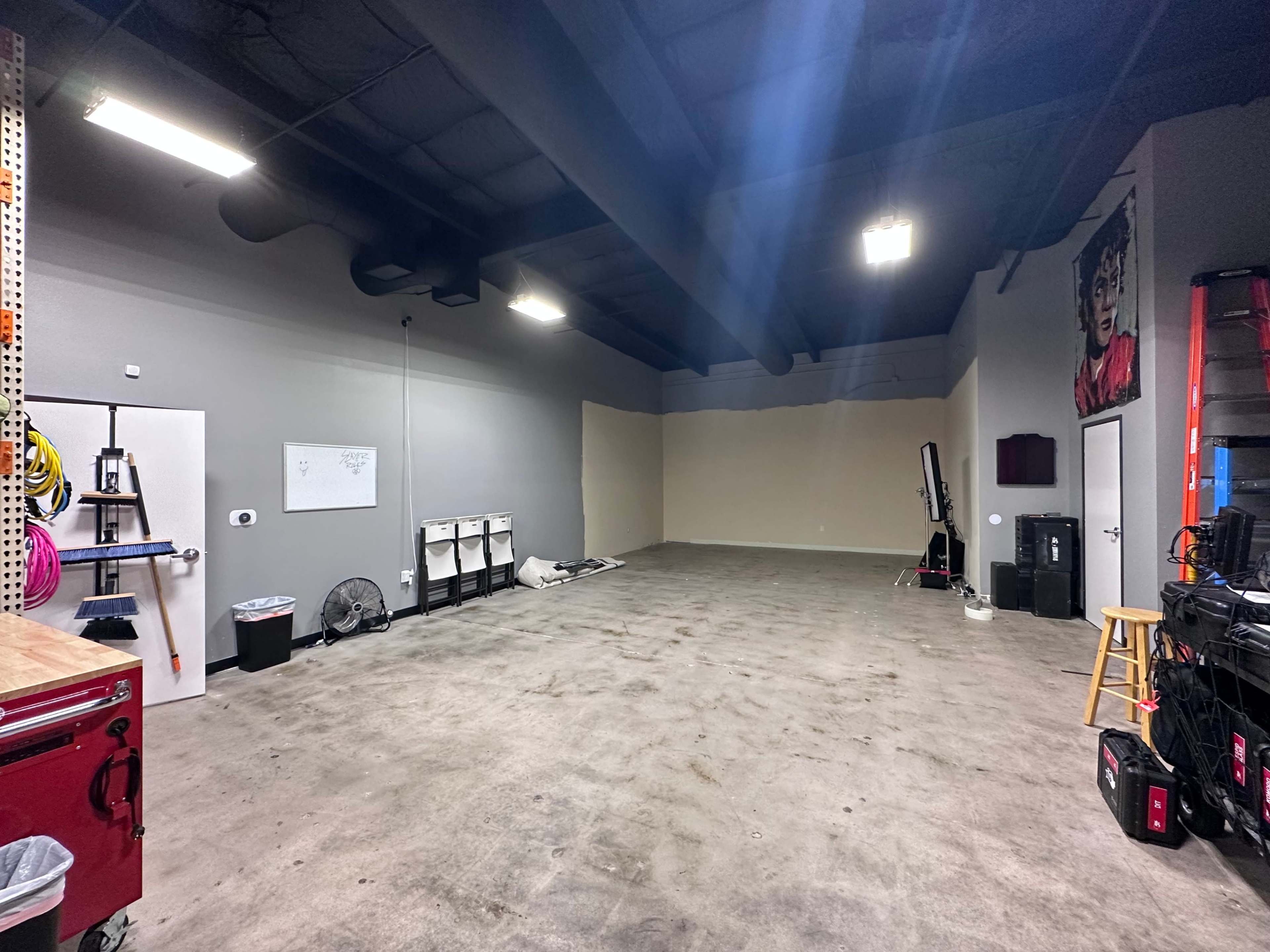 A spacious, empty garage or workshop with concrete flooring and unfinished walls, featuring a few storage units and tools along the perimeter.