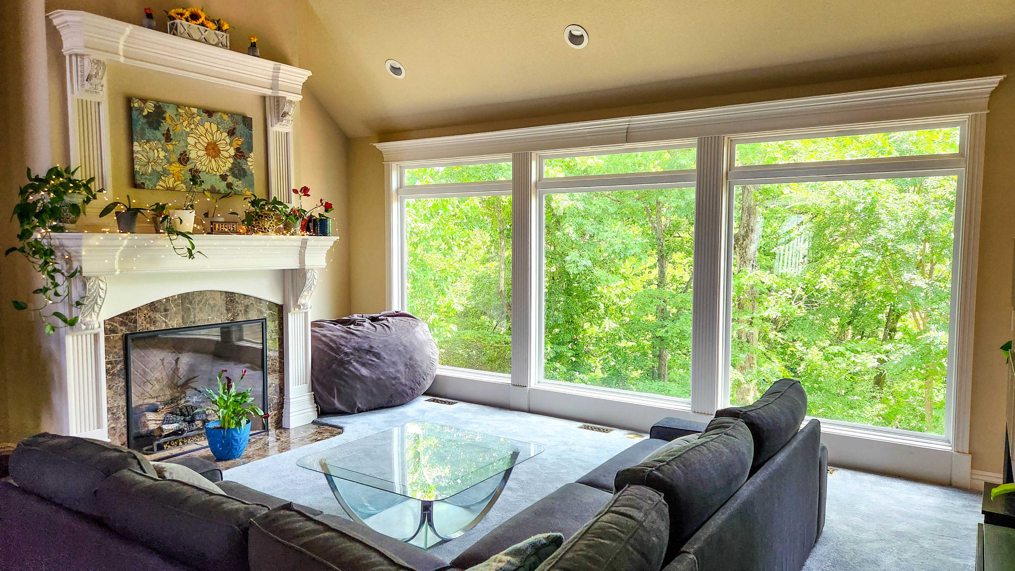 A living room features a large window with views of greenery, a fireplace with decorative items, and a seating area with a glass coffee table.