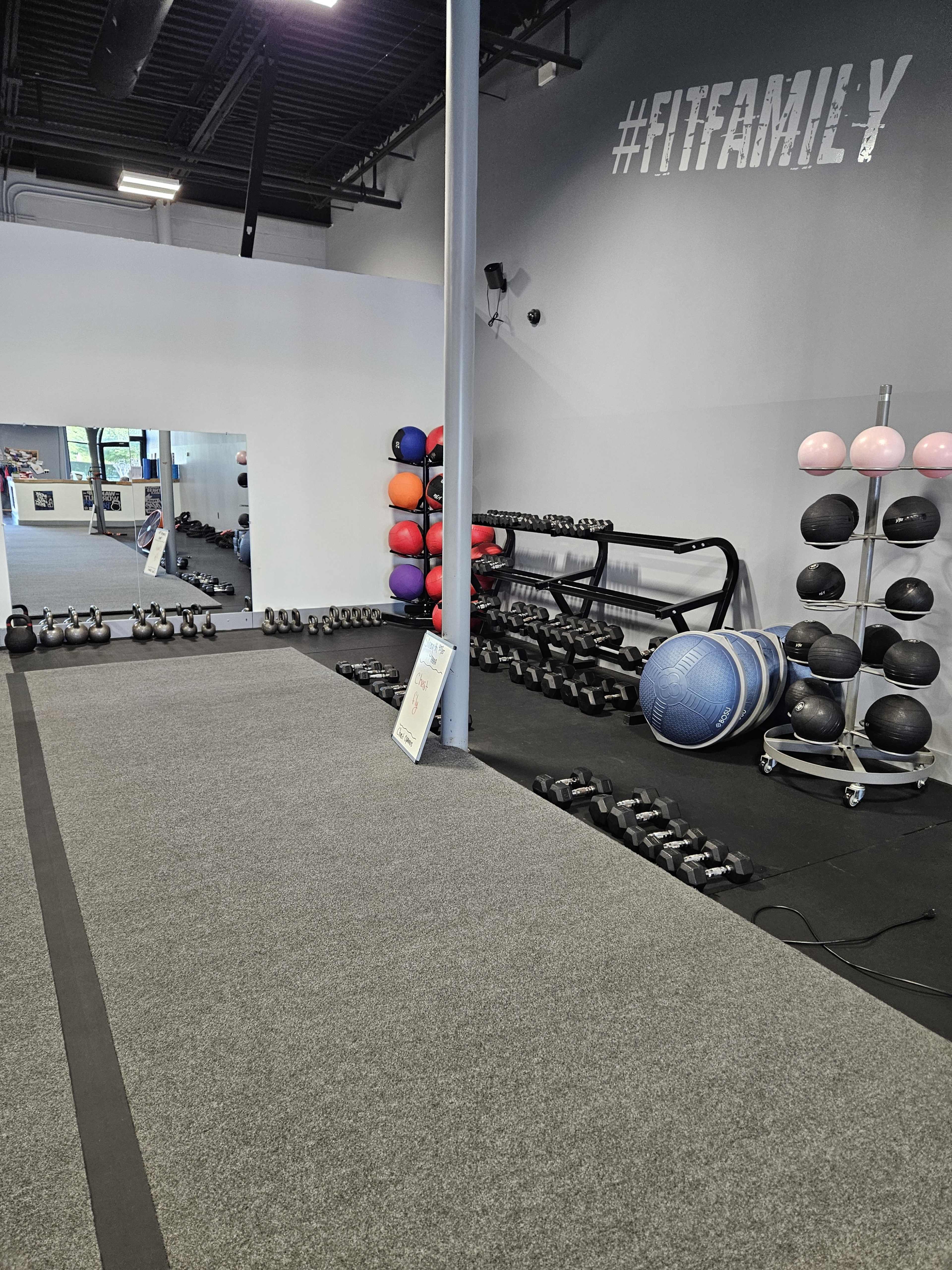A gym area features various weights, exercise balls, and a mirrored wall, with a motivational "#FITFAMILY" mural above.
