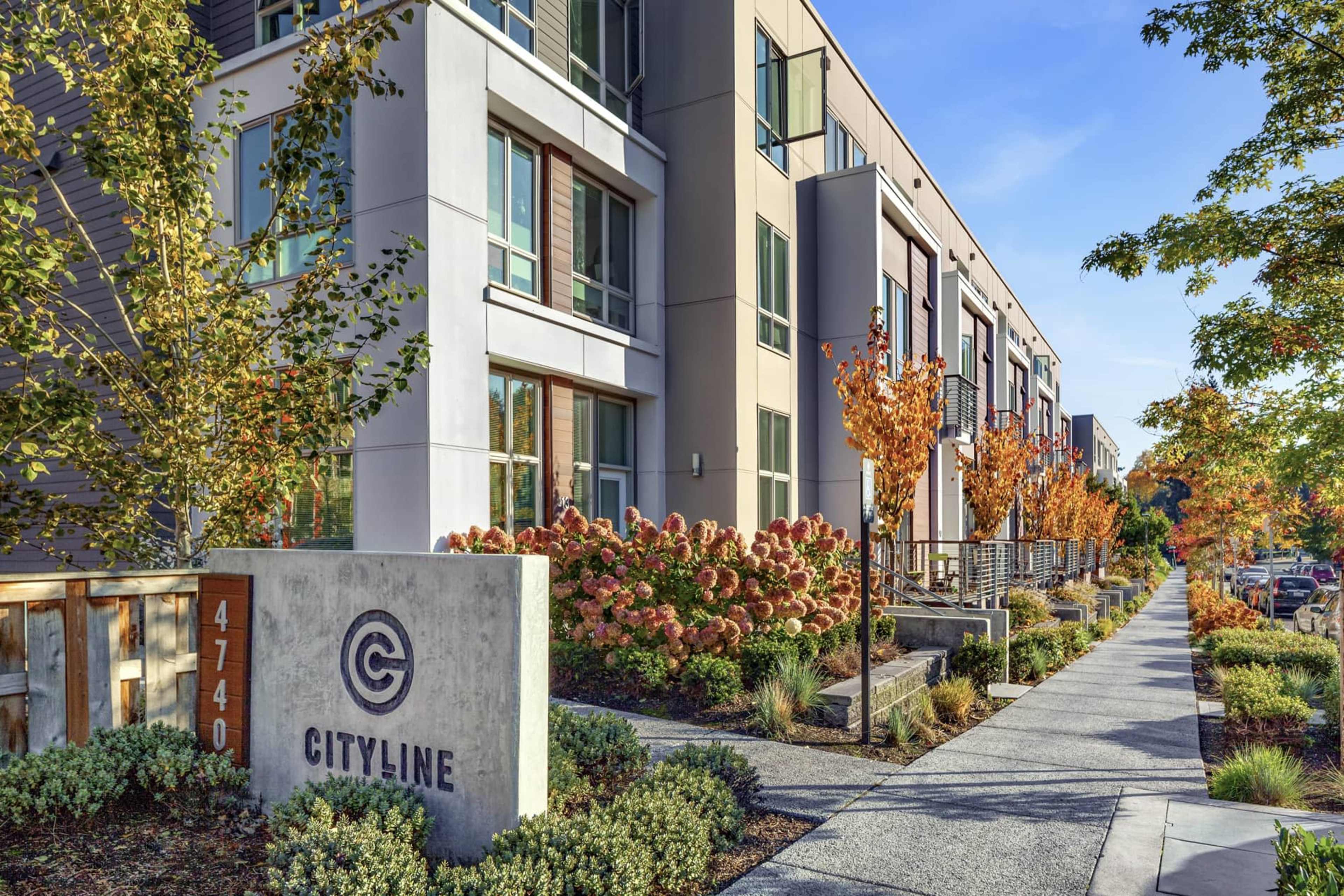 A modern apartment complex named "Cityline," featuring a landscaped path lined with trees and flowering shrubs.