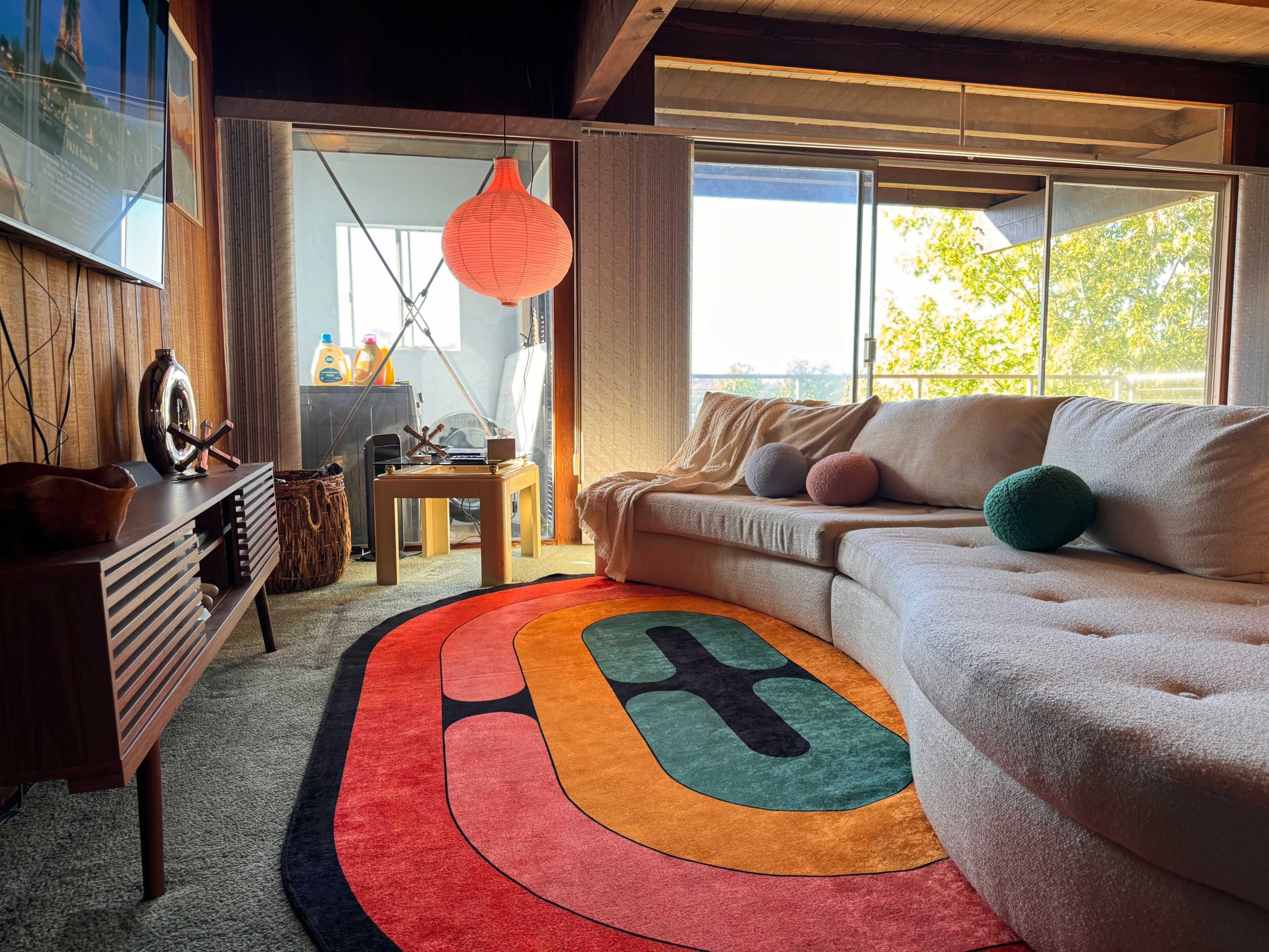 A cozy living room features a large sectional sofa, a colorful area rug, and a window with natural light streaming in.