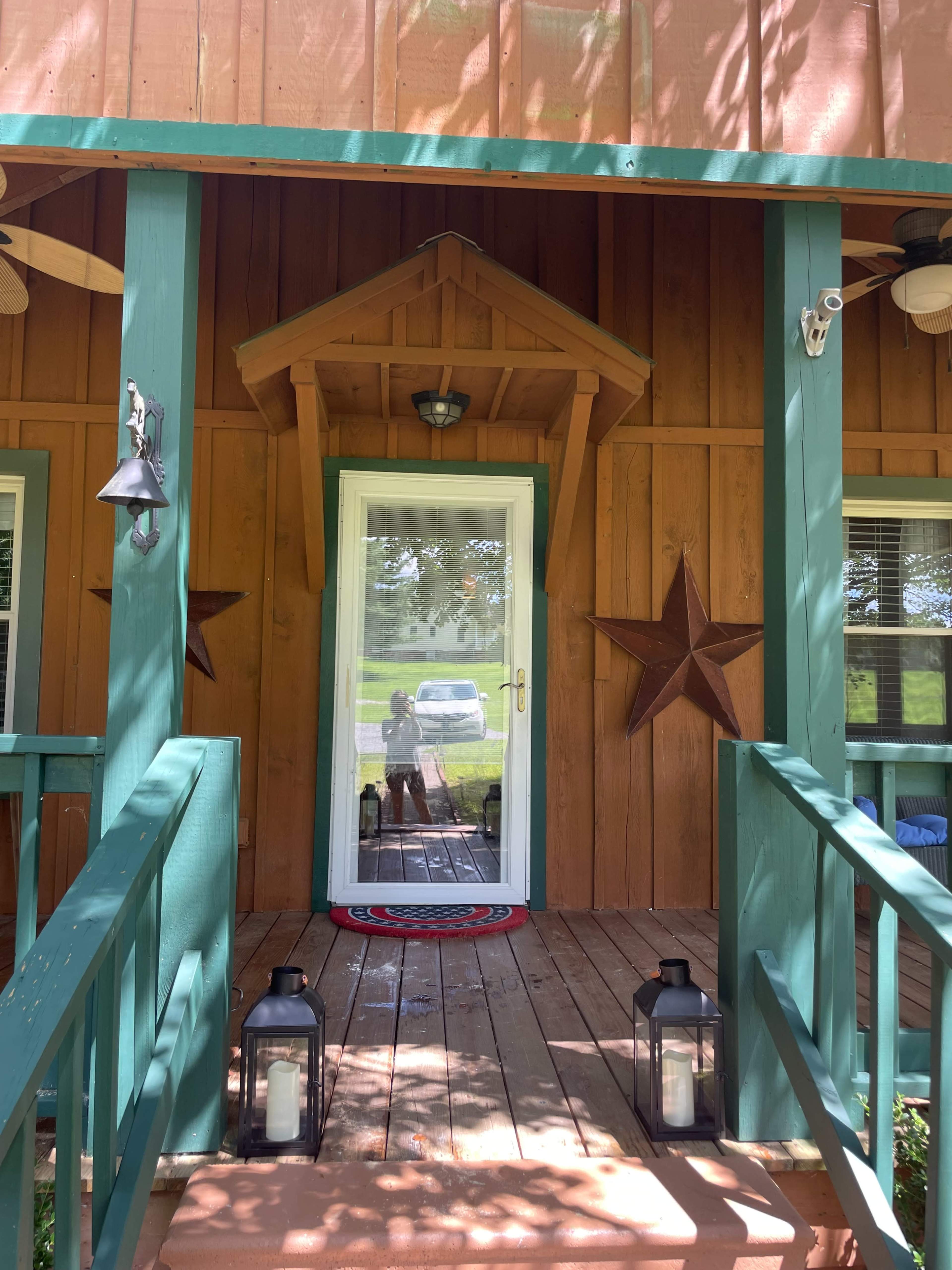 The image shows a wooden porch with green railings, star decorations on the walls, and a white door leading inside.