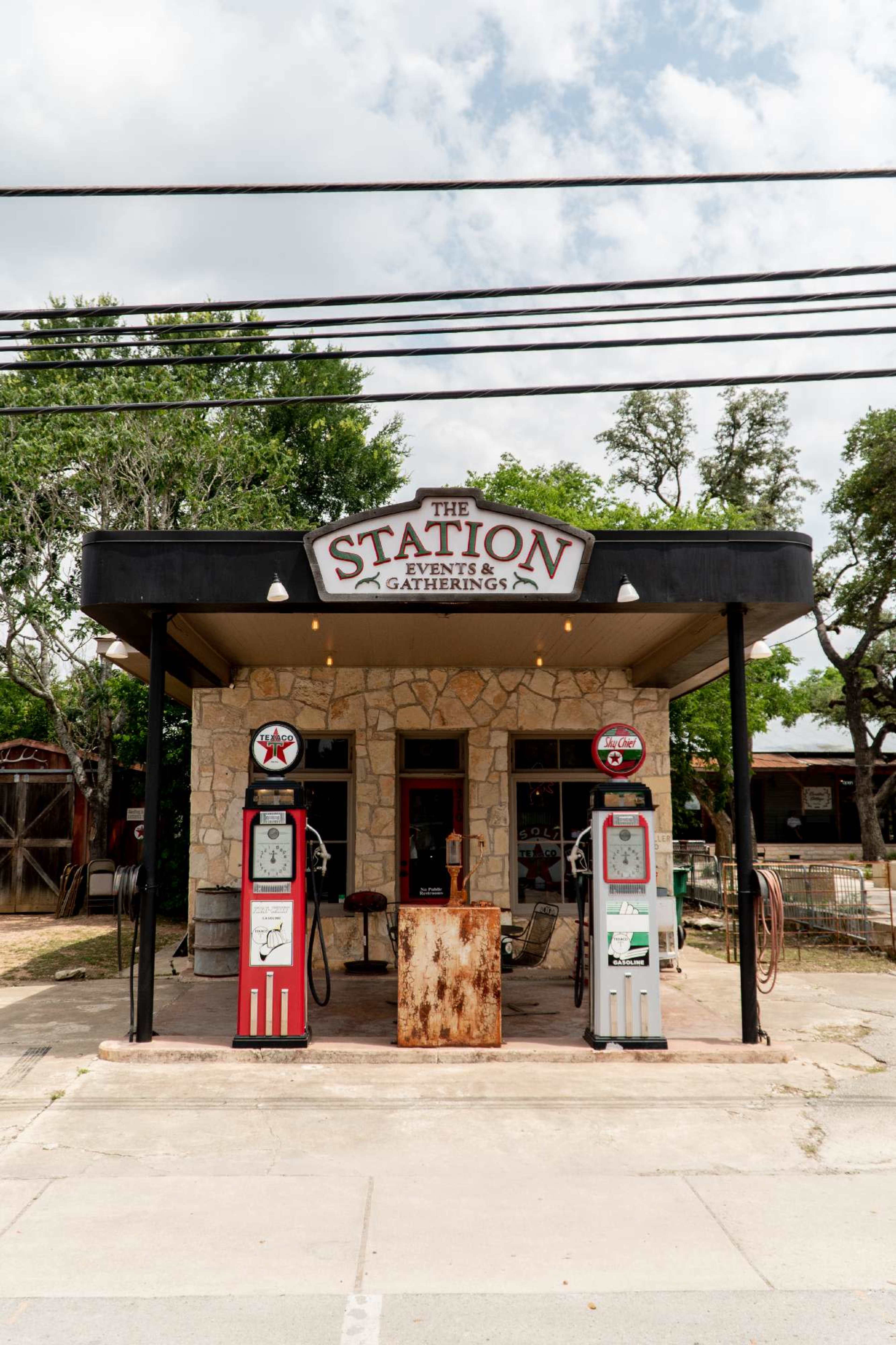 A building labeled "The Station Events & Gatherings" features vintage gas pumps at the entrance, surrounded by greenery and power lines.