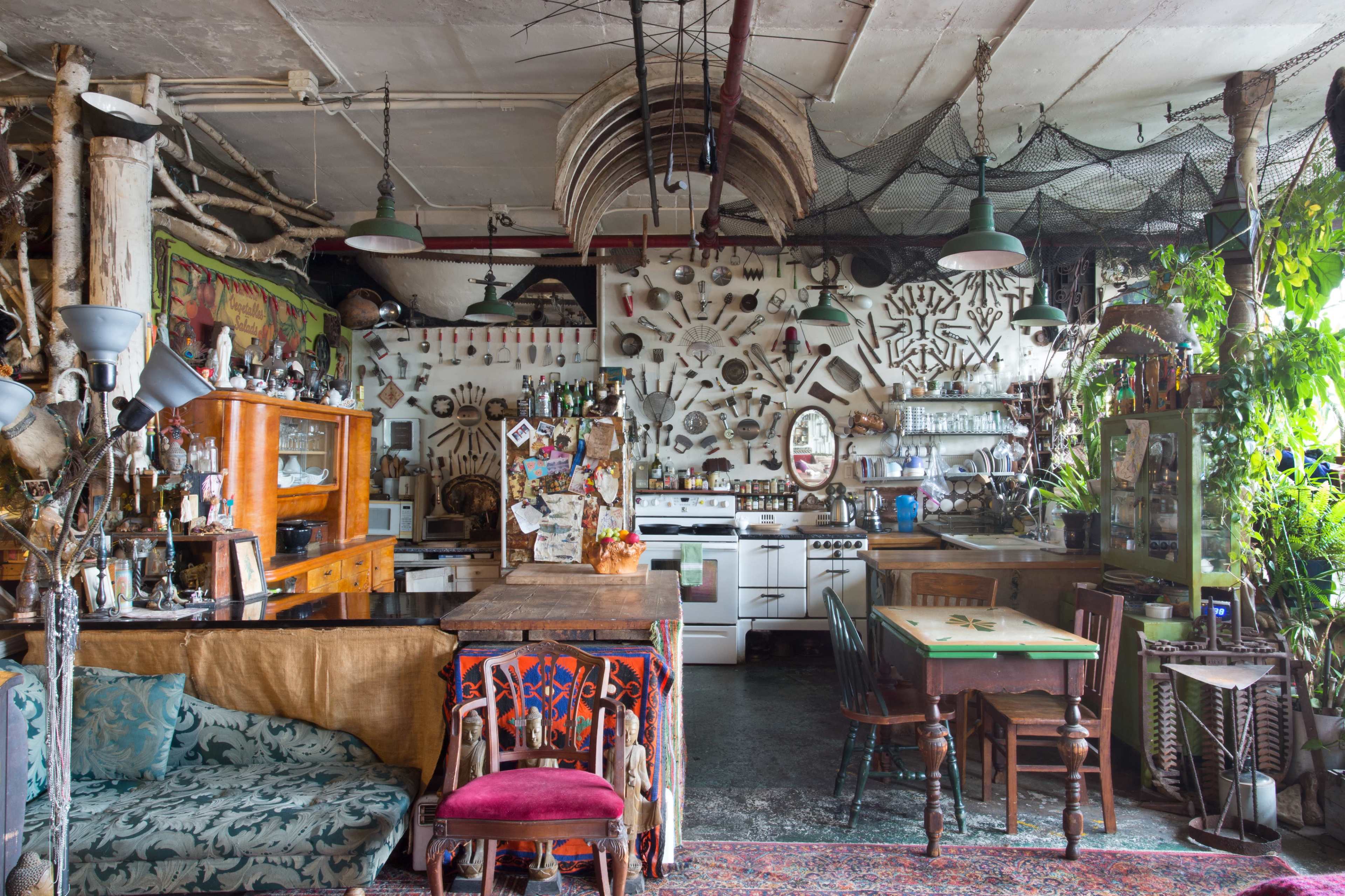 An eclectic kitchen and dining area filled with various objects, decor, and furniture, including a wooden table, chairs, and multiple wall-mounted items.