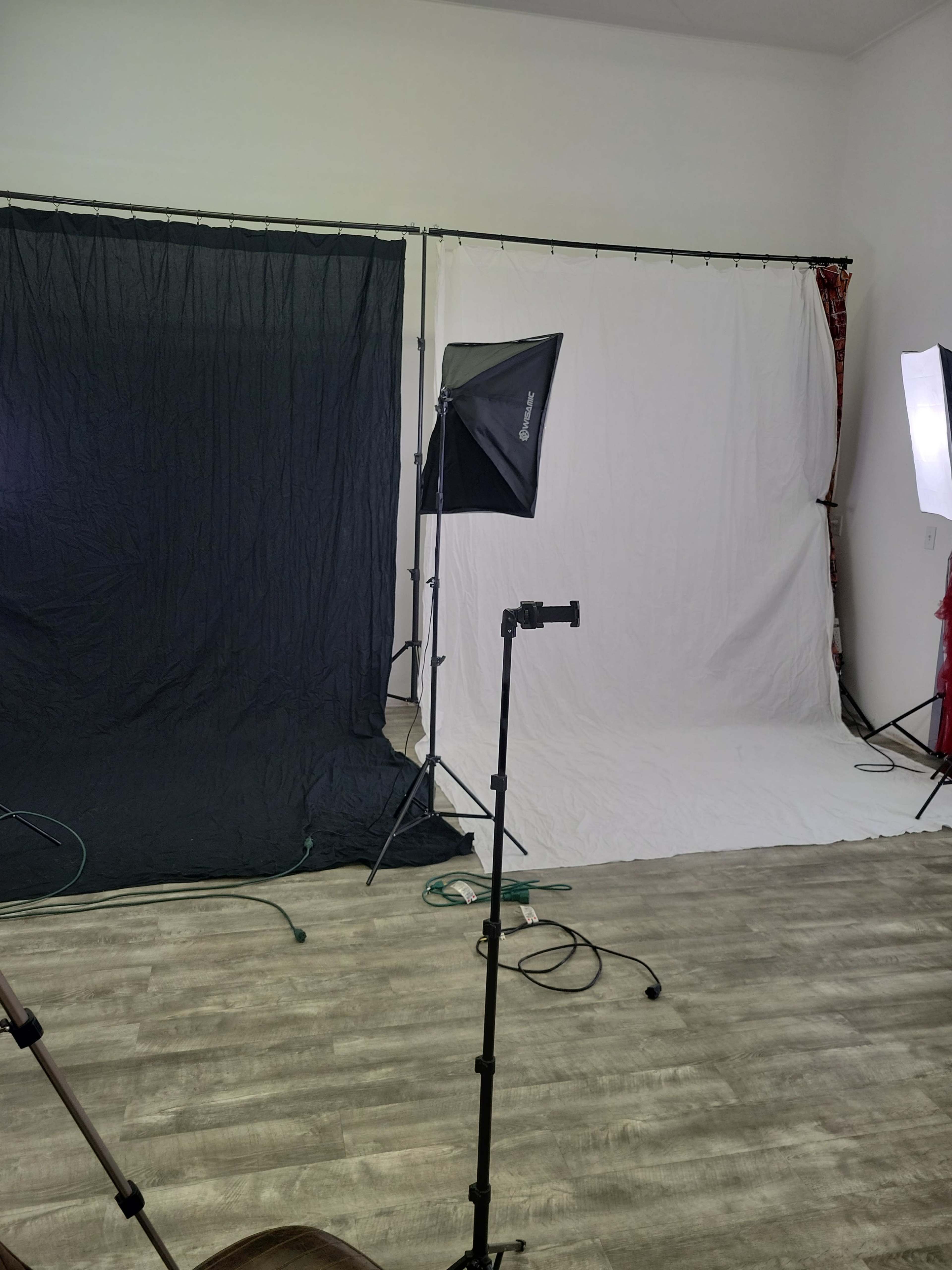 The image shows a photography studio with a black backdrop to the left and a white backdrop to the right, accompanied by various lighting equipment.