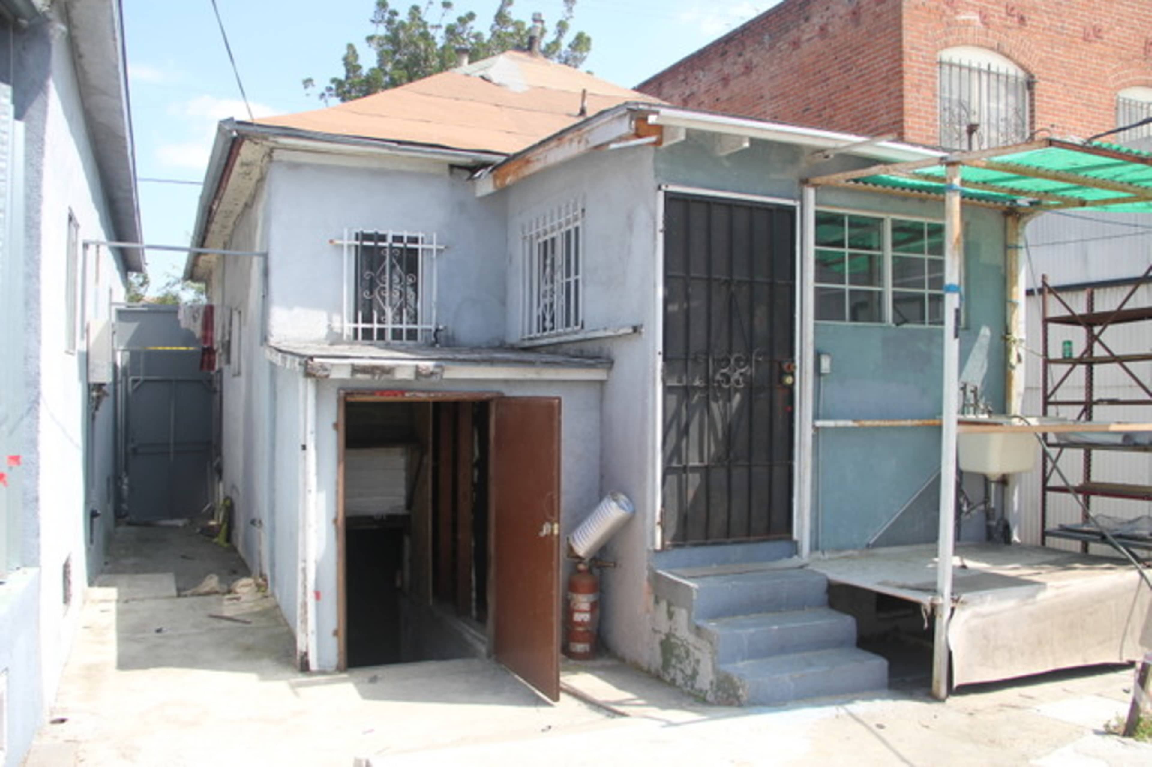 A small, single-story house with a distinct entrance, set against a backdrop of neighboring buildings.