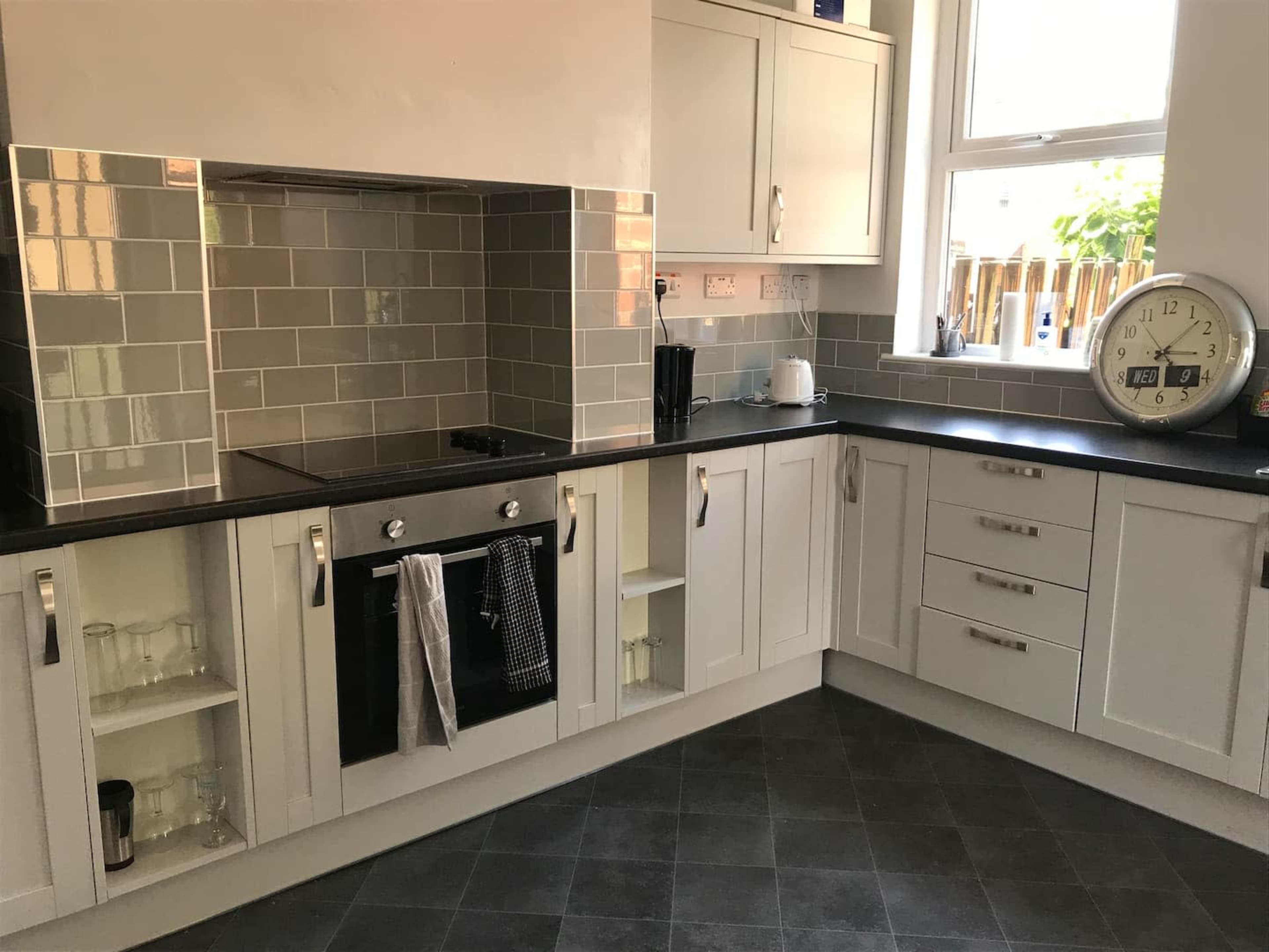 A modern kitchen features gray tiled backsplash, a black countertop, and white cabinetry with an oven and clock on display.