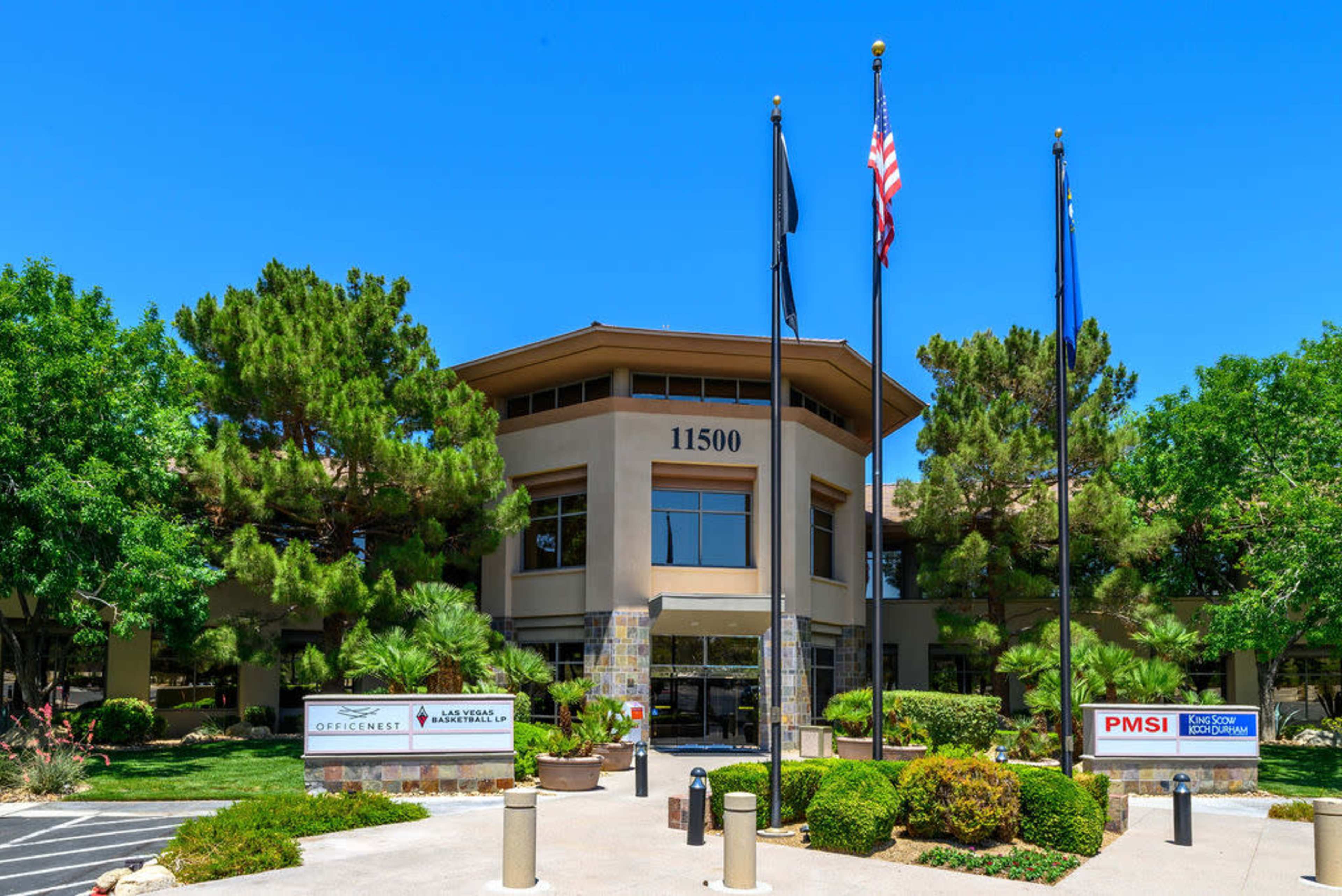 A multi-story office building with several flags flying in front and lush greenery surrounding the entrance.
