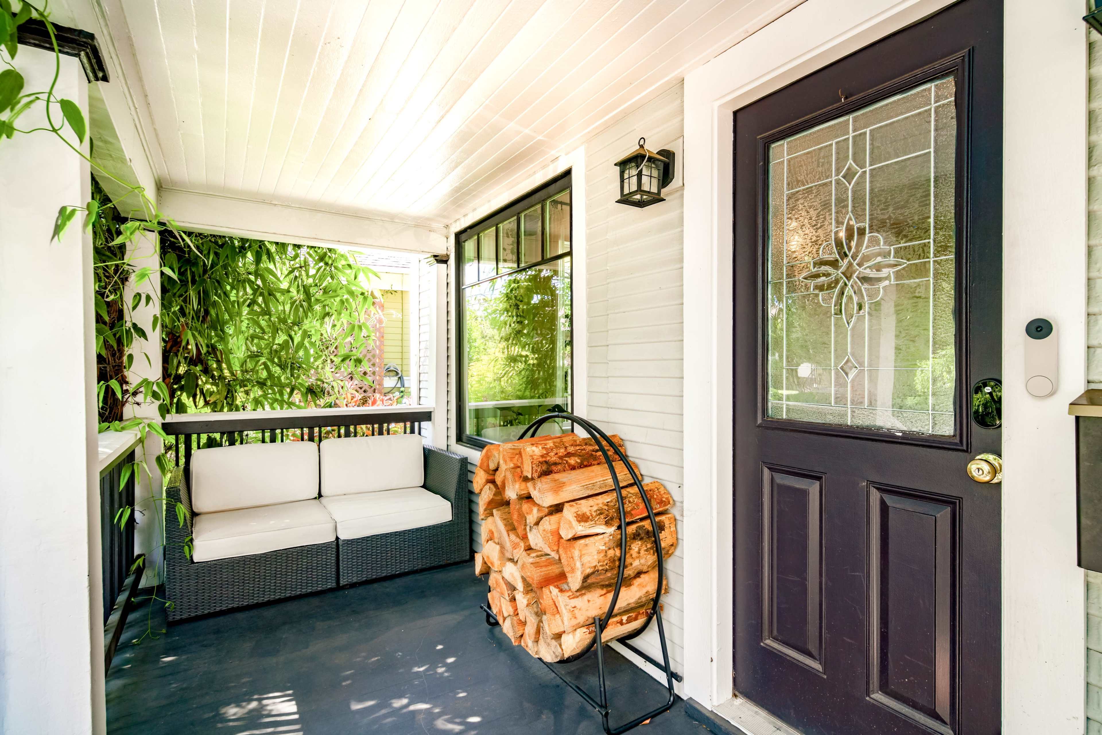 The image shows a porch with a small seating area beside a stack of firewood and a decorative door.