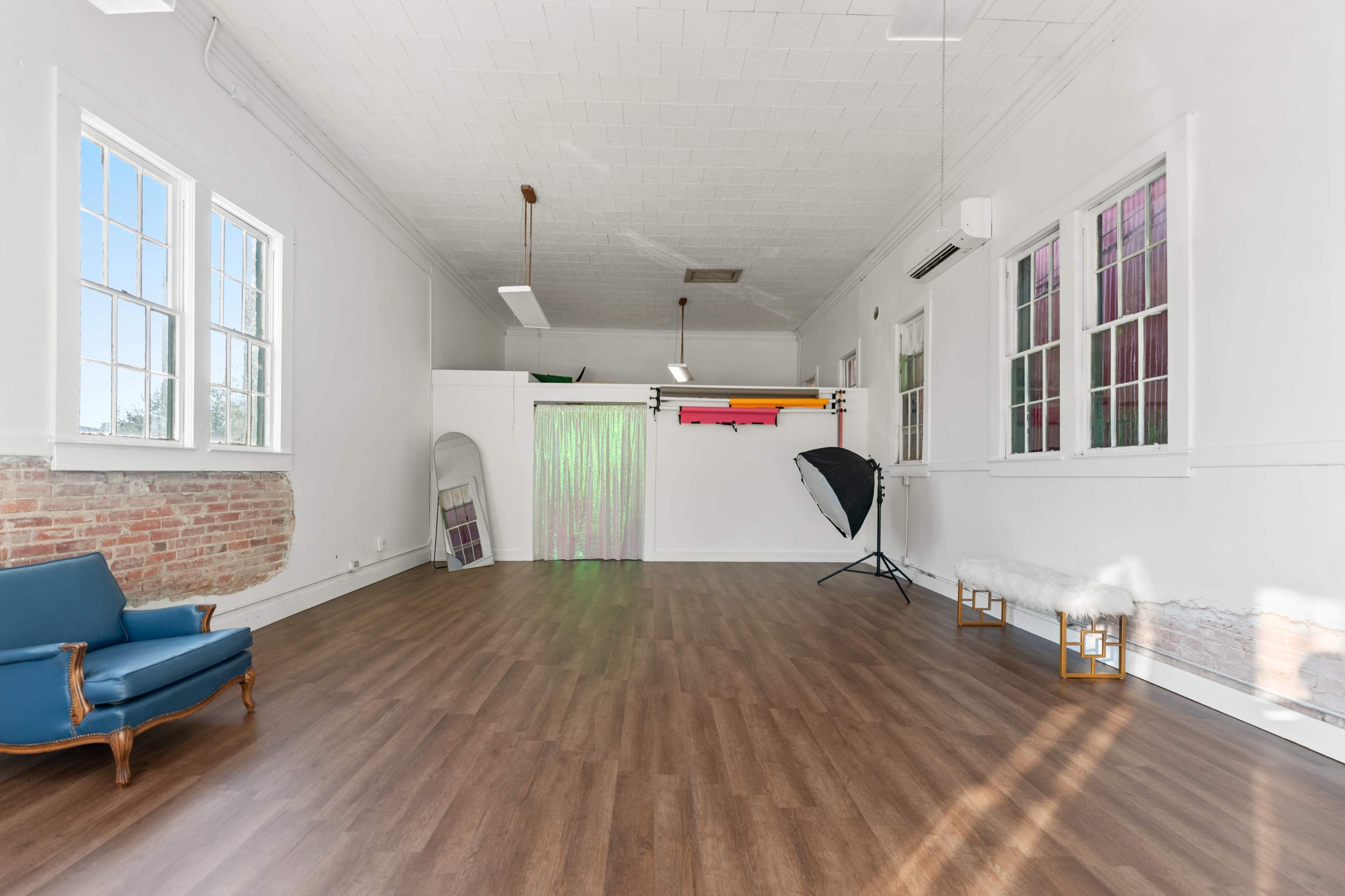 The room features a spacious, light-filled interior with wooden flooring, a variety of colored backdrops, and a seating area in the corner.