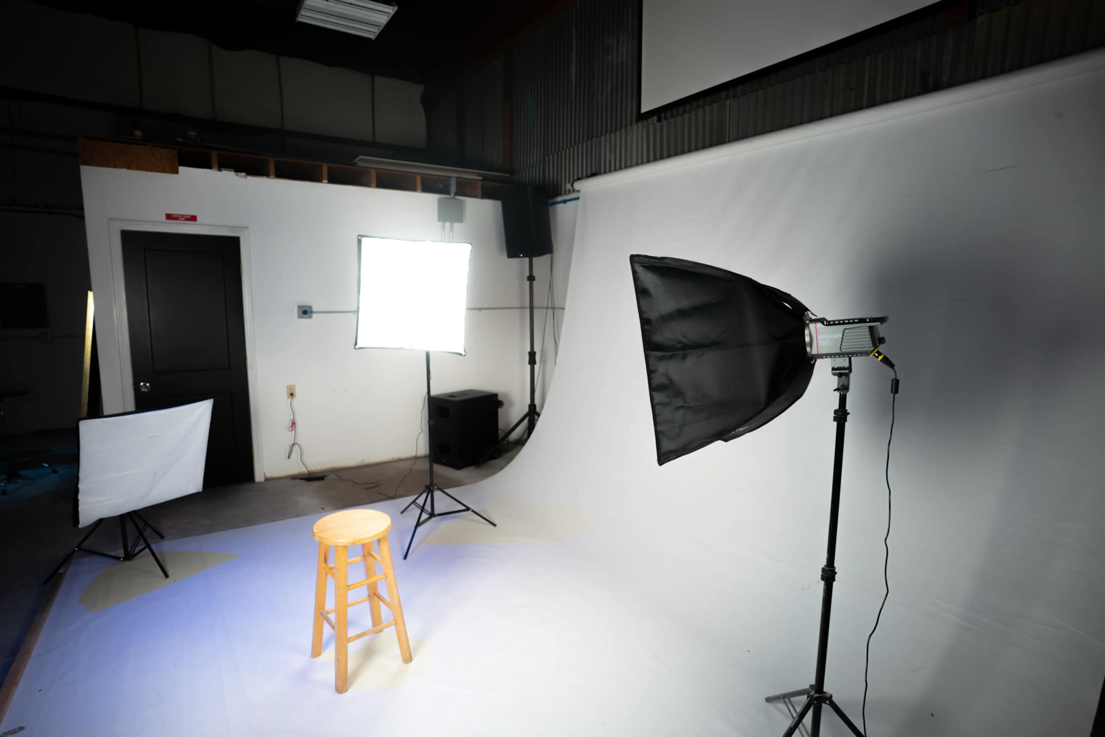 A photography studio setup featuring a wooden stool in front of a white backdrop, with multiple softbox lights positioned around it.