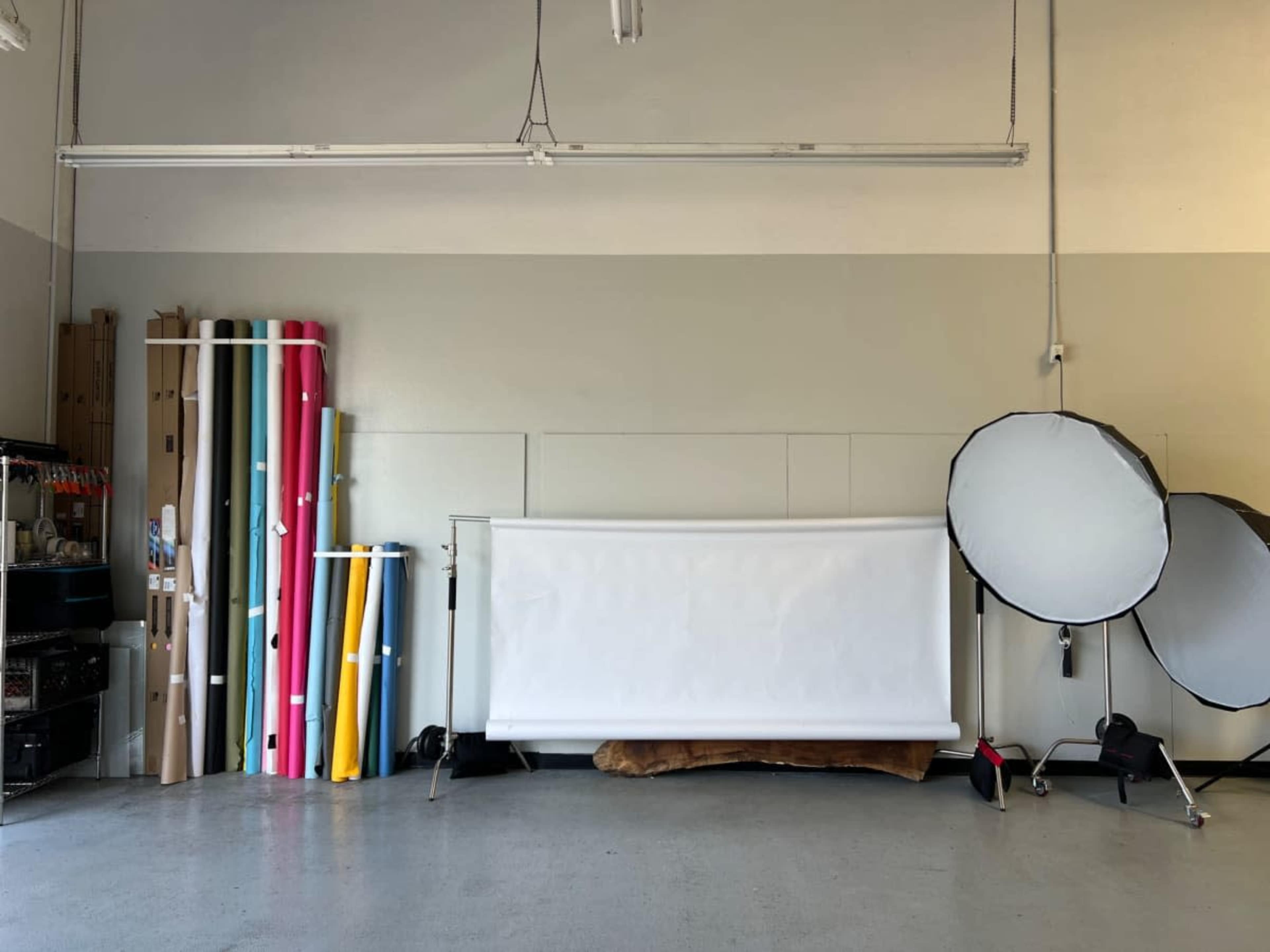 The image shows a spacious studio with rolls of colored backdrop materials on the left and photography equipment, including two reflectors, on the right.