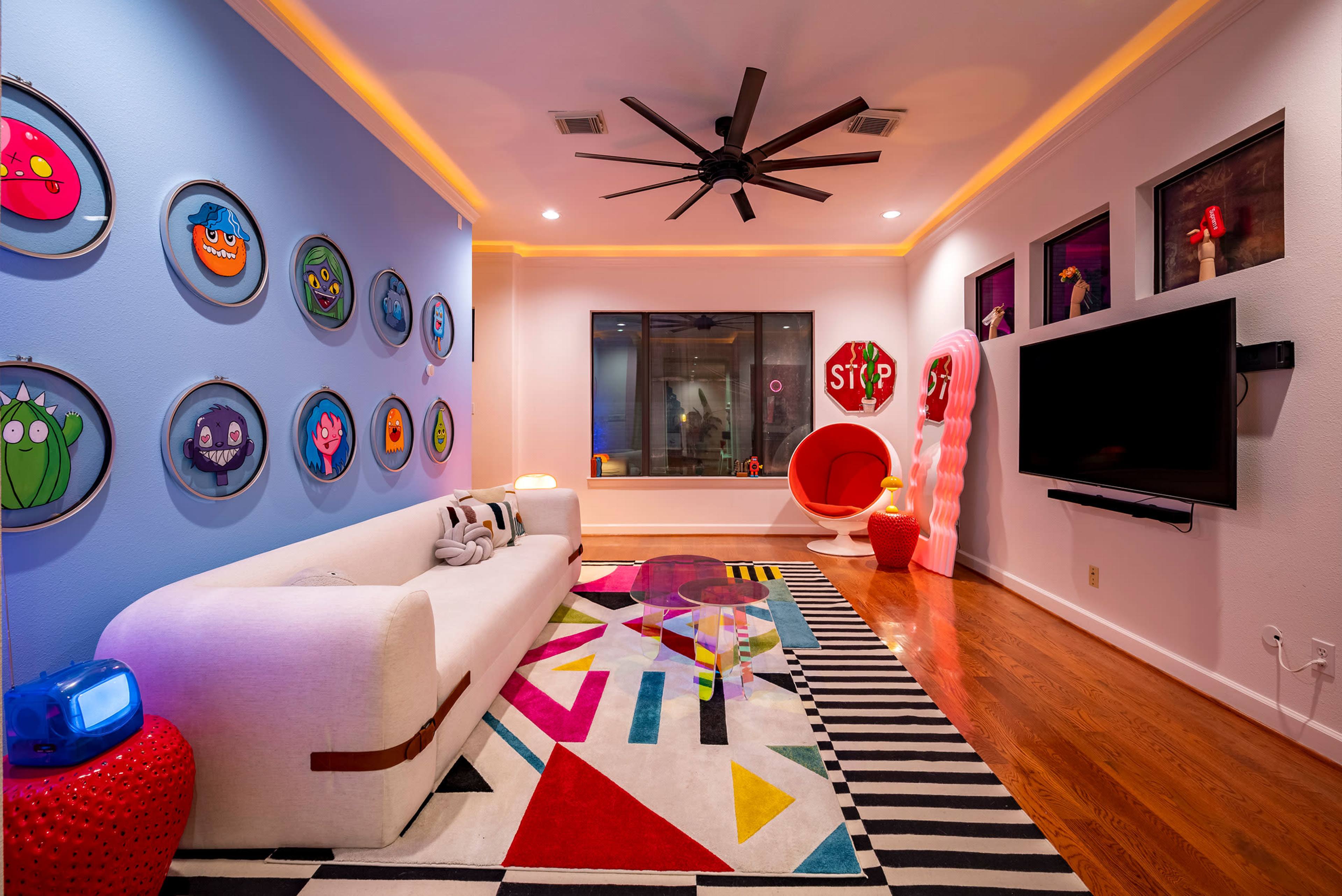 The room features a colorful modern design with a white sofa, a bold area rug, framed artwork on the walls, and a large window.