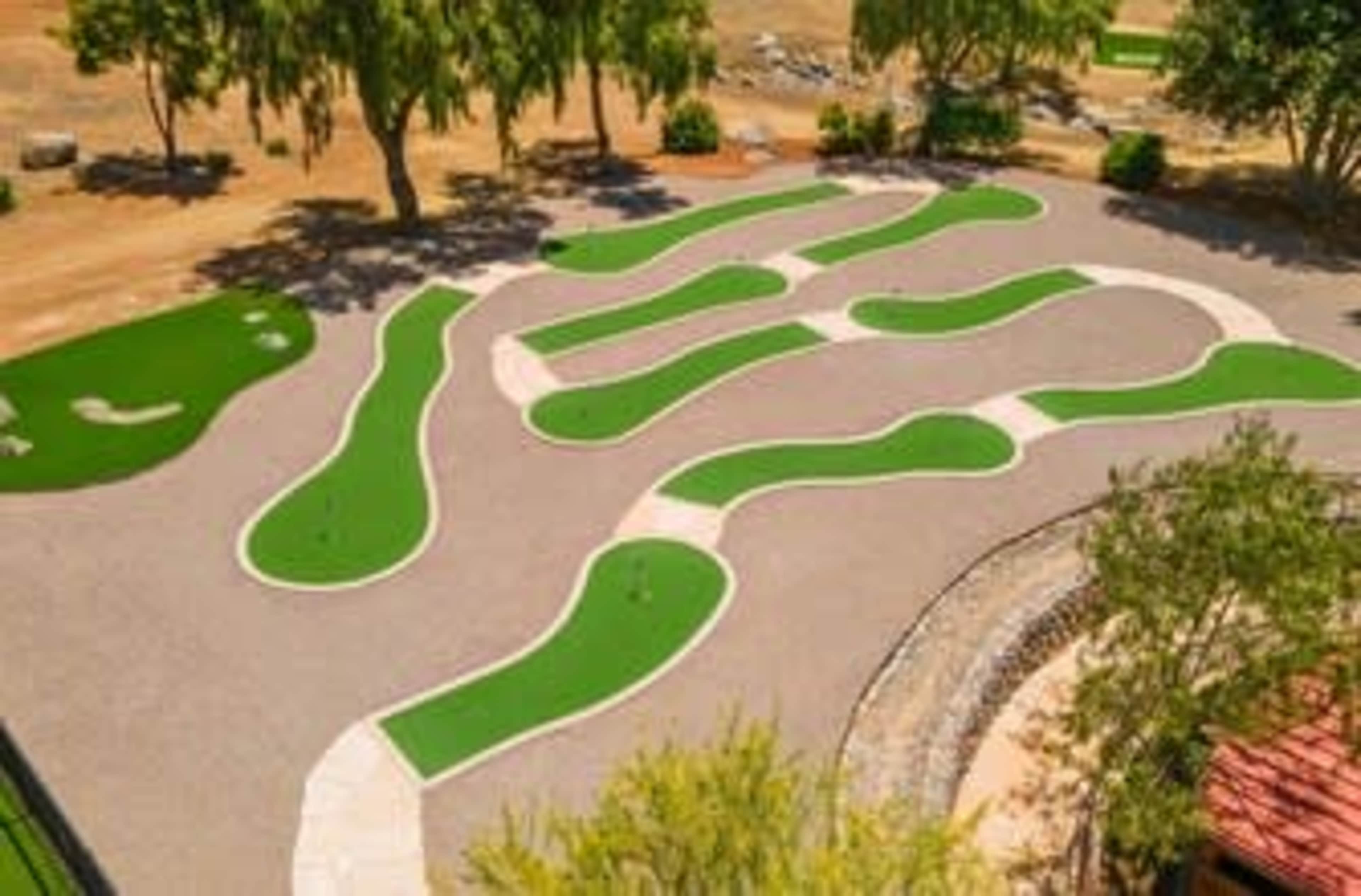 A miniature golf course with winding green putting areas set among gravel paths and trees.