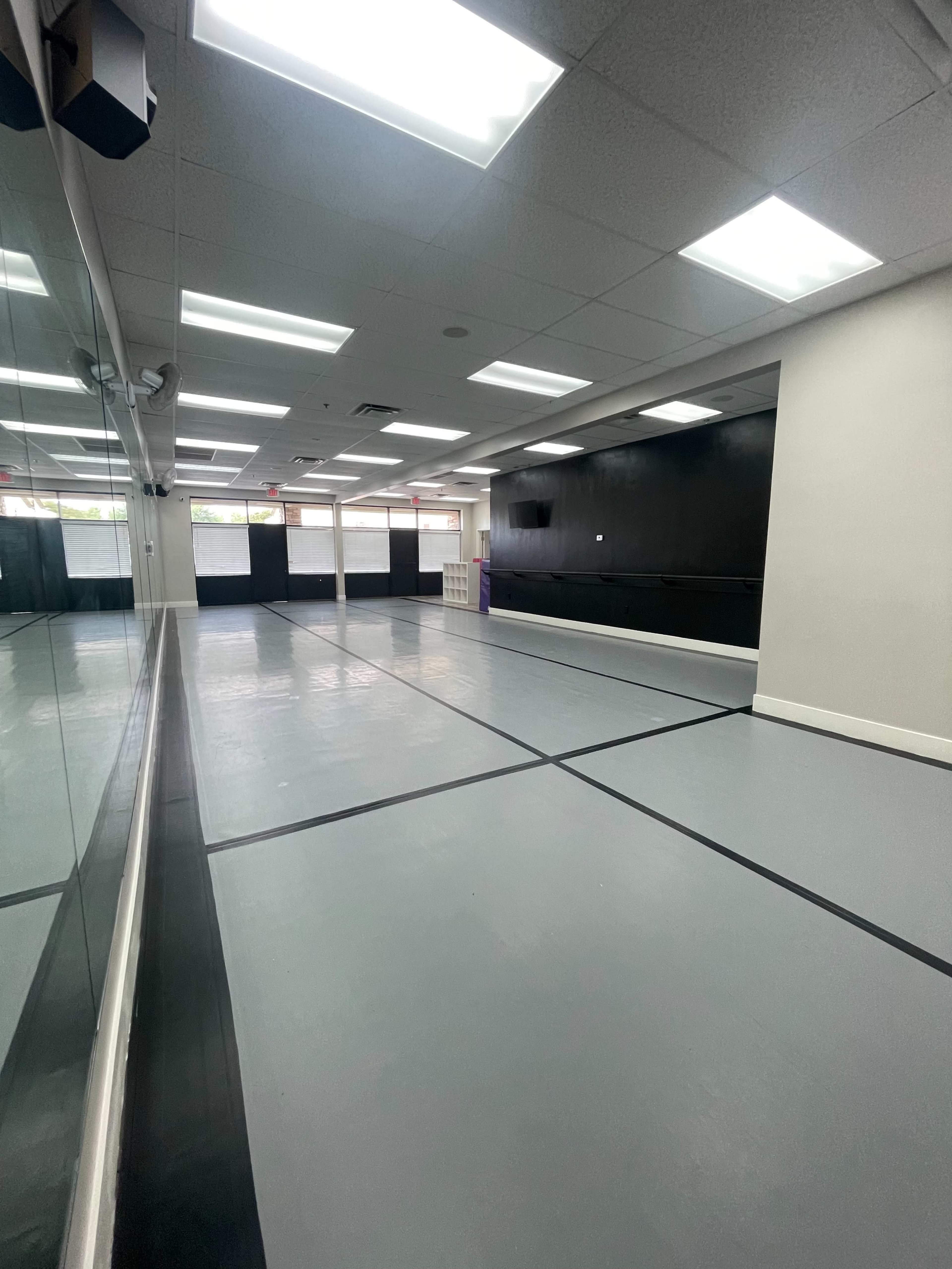 An empty studio space with a gray floor, mirrored walls, and overhead lighting.
