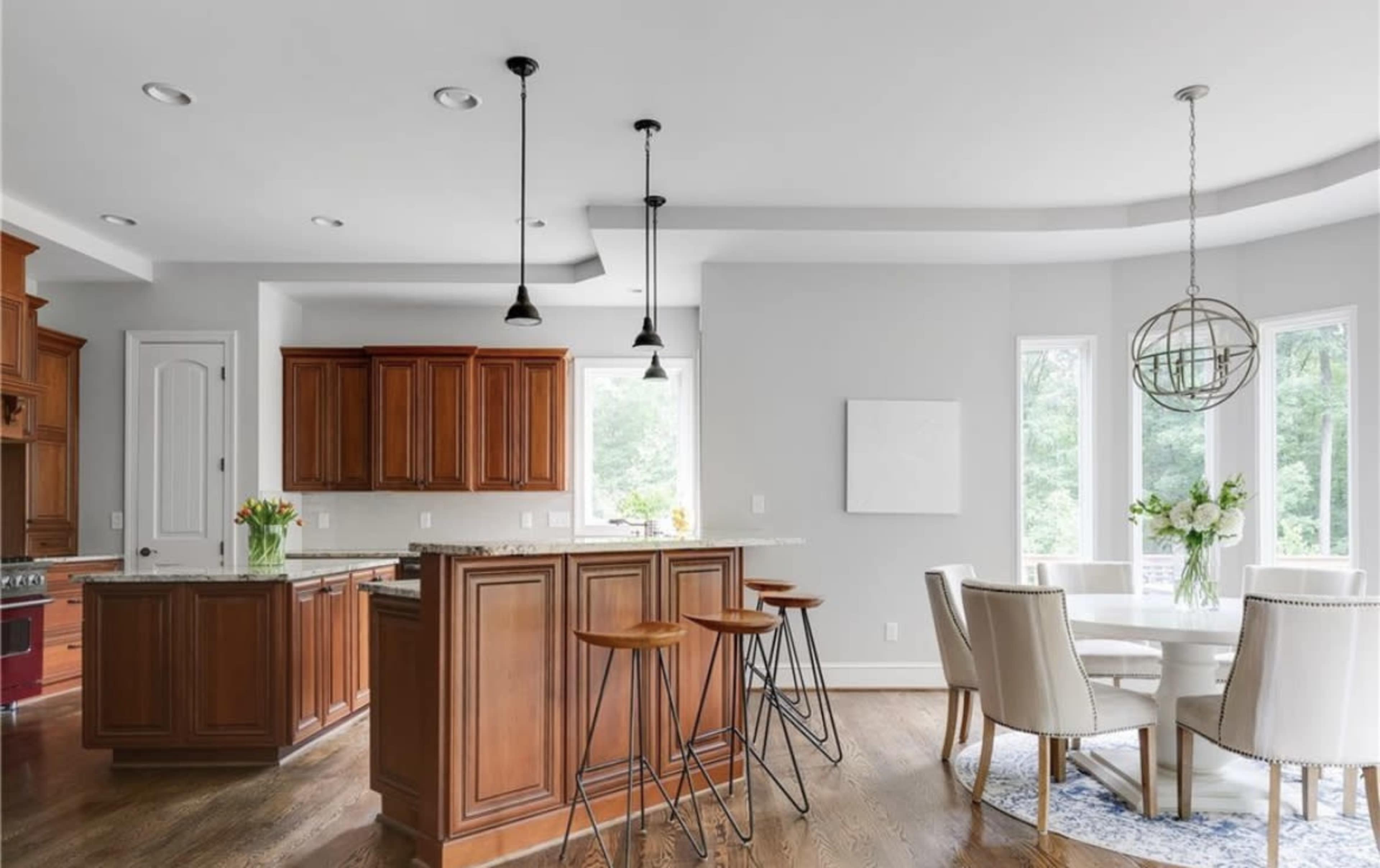 A modern kitchen features dark wooden cabinetry, a large island with bar stools, and a dining area with a round table and upholstered chairs.
