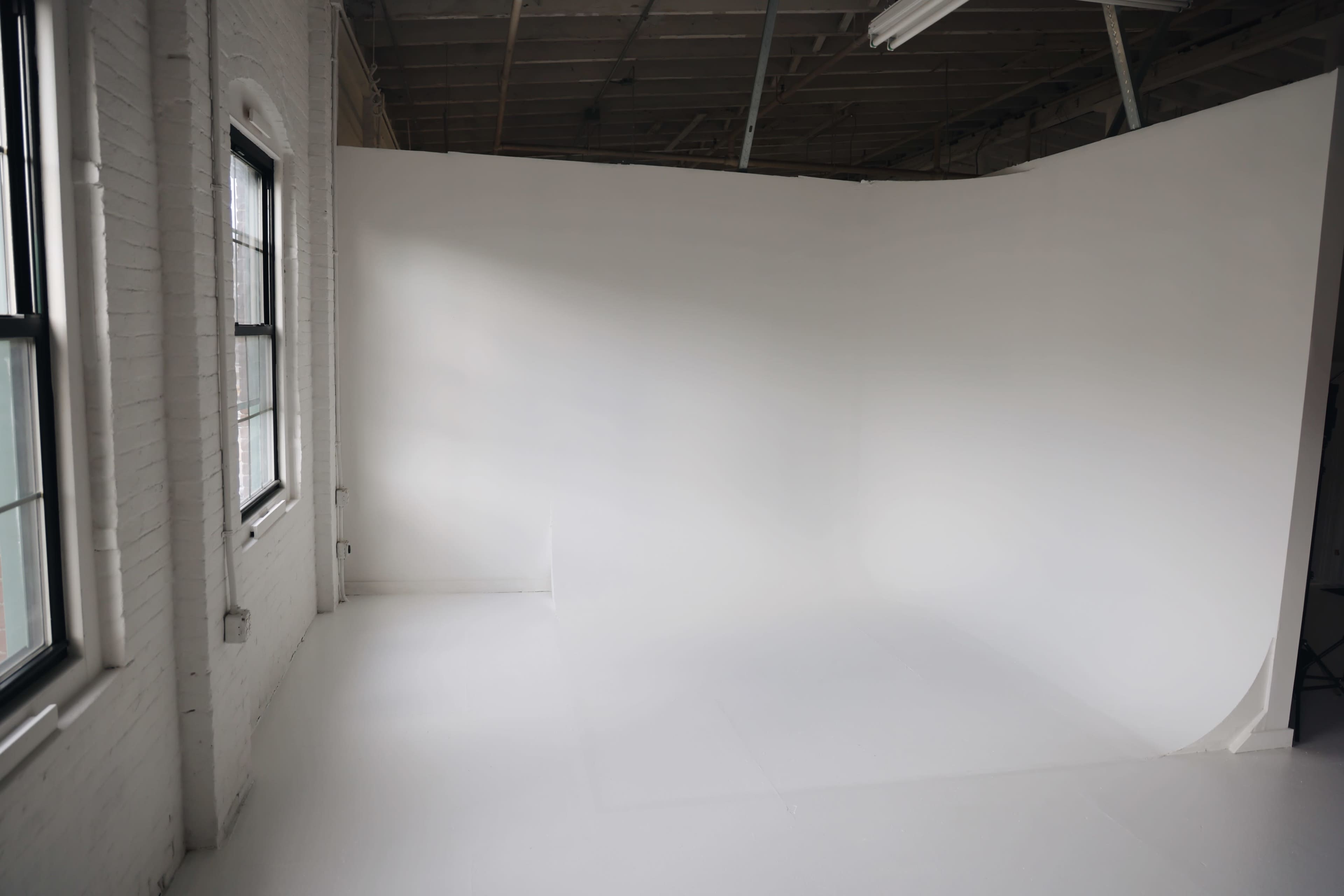 An empty, well-lit studio space with white walls and a seamless white floor.