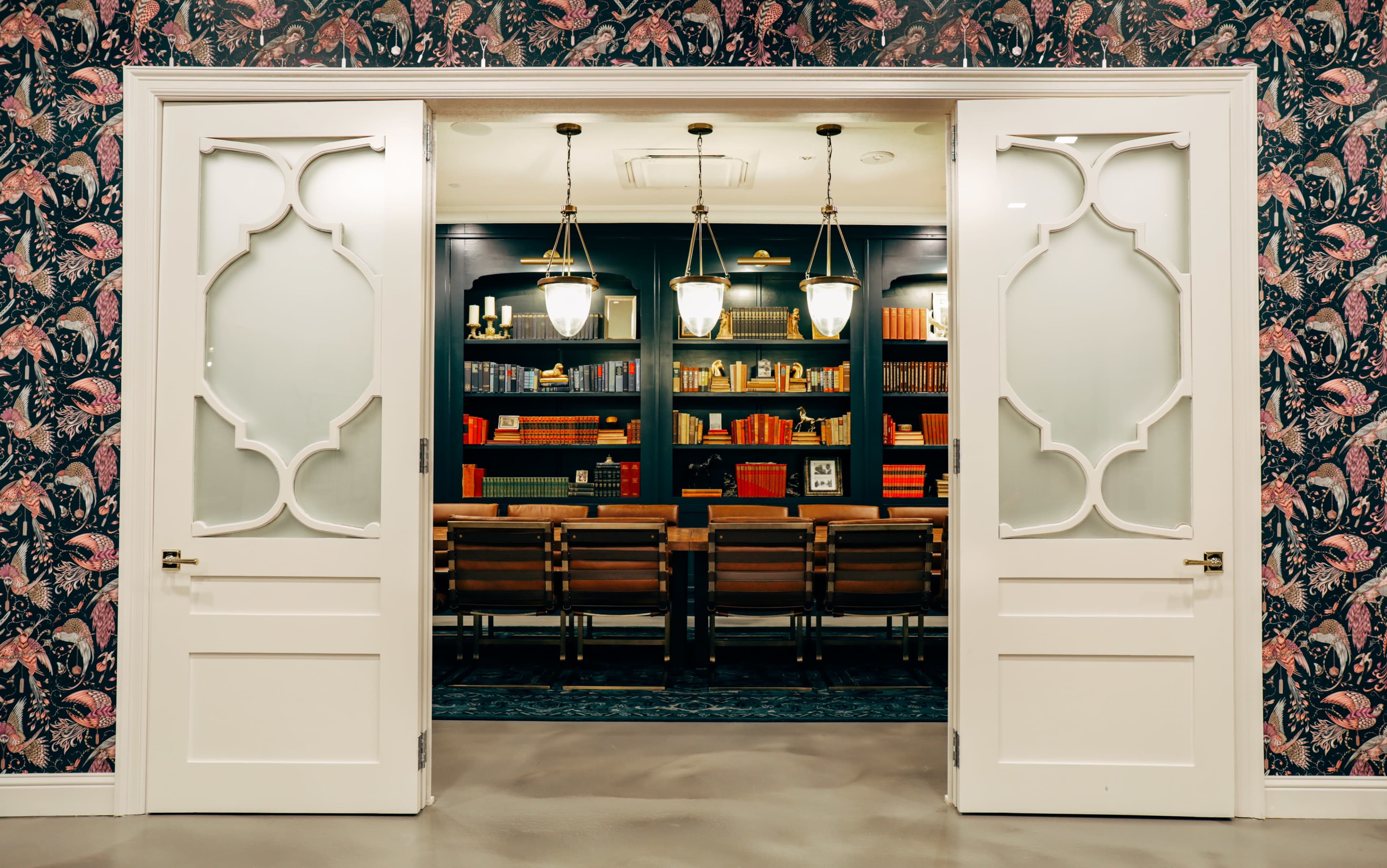A set of double doors framed by ornate patterns opens to a room with a long wooden table and shelves filled with books.