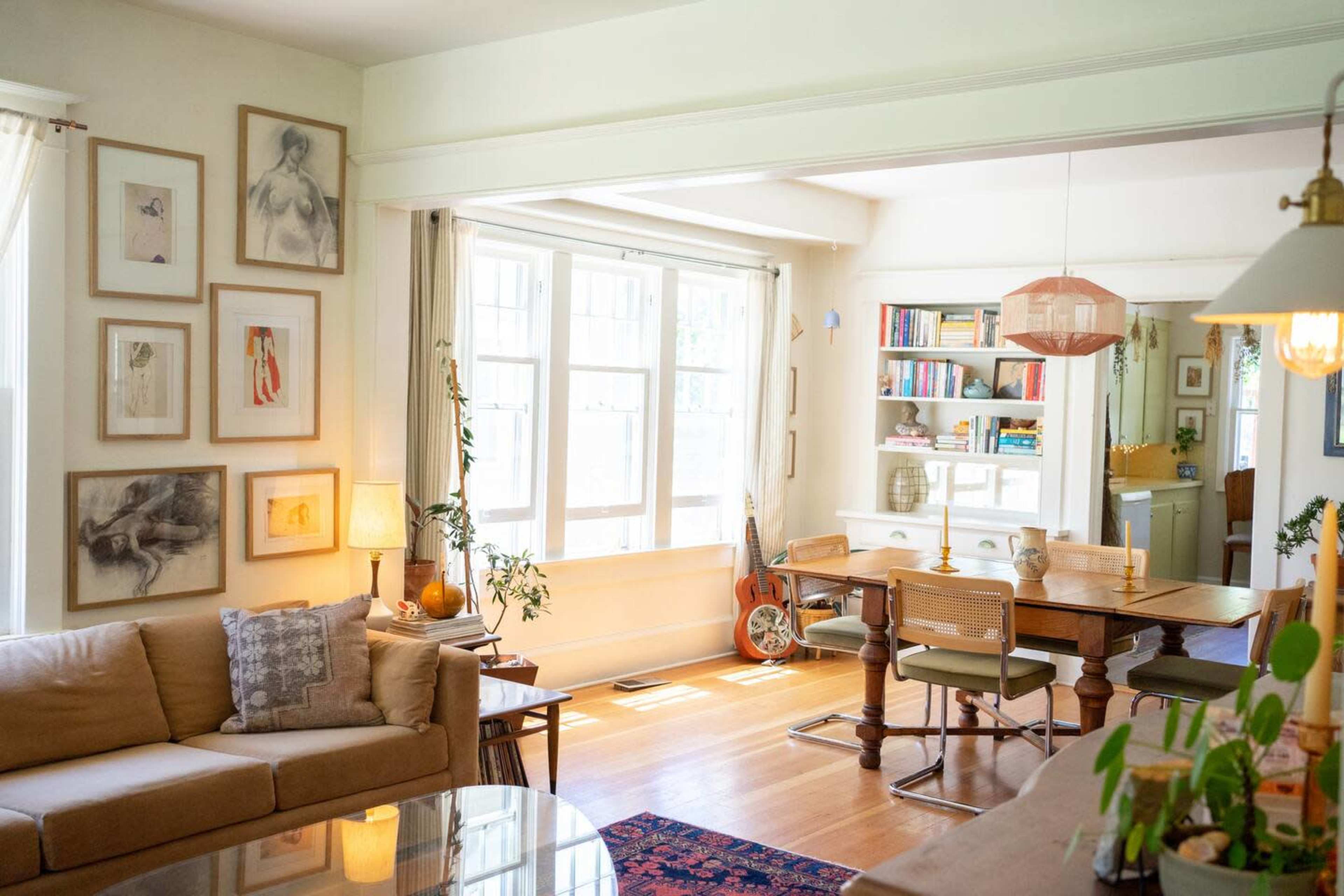 A bright living space with a beige couch, a wooden dining table, and large windows allowing natural light to fill the room.