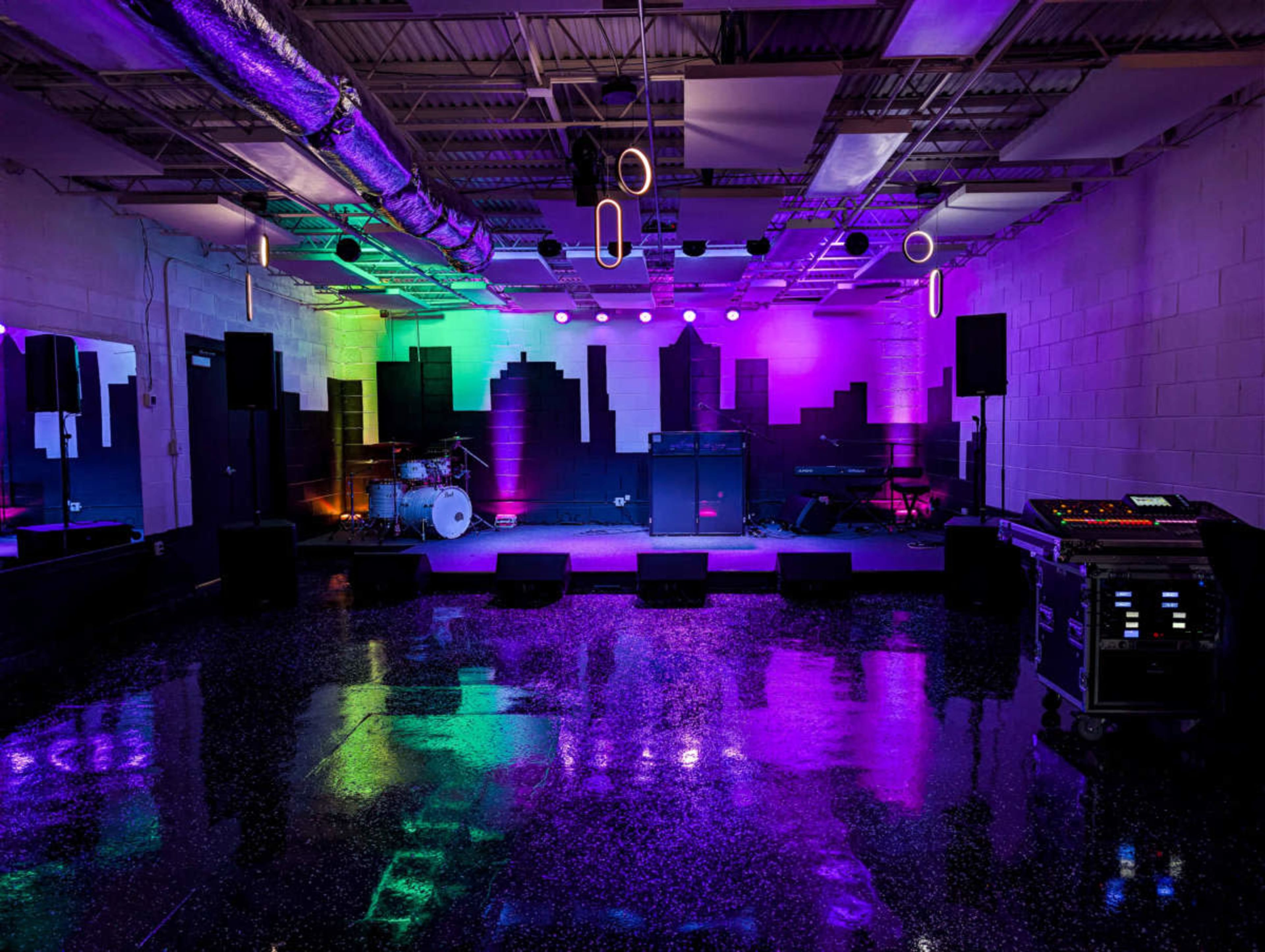 The image shows a music performance space with a stage, musical instruments, and colorful lighting reflecting off the shiny floor.