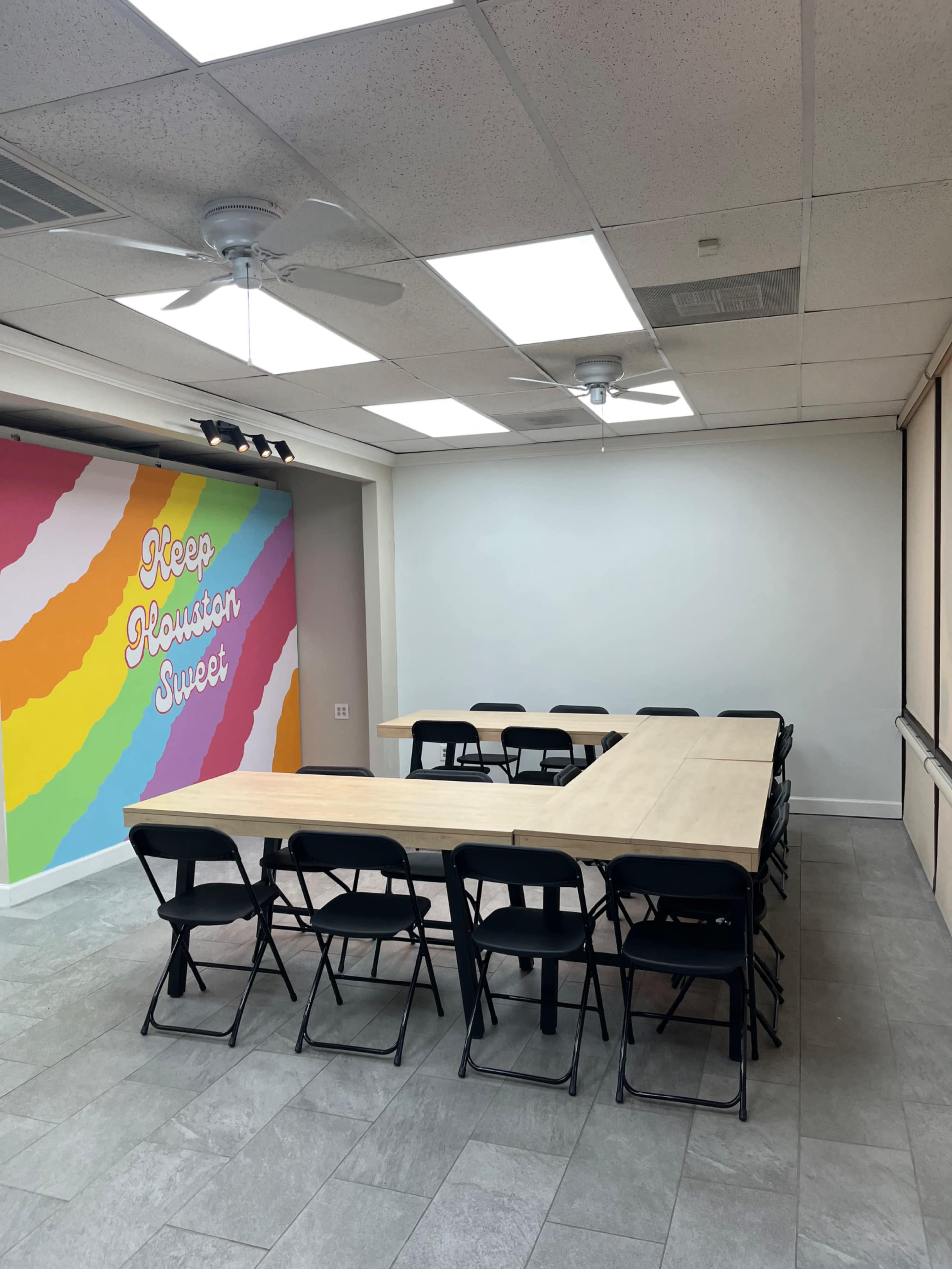 The image shows a meeting room with a U-shaped table arranged with black chairs, and a colorful mural on one wall that reads "Keep Houston Sweet."