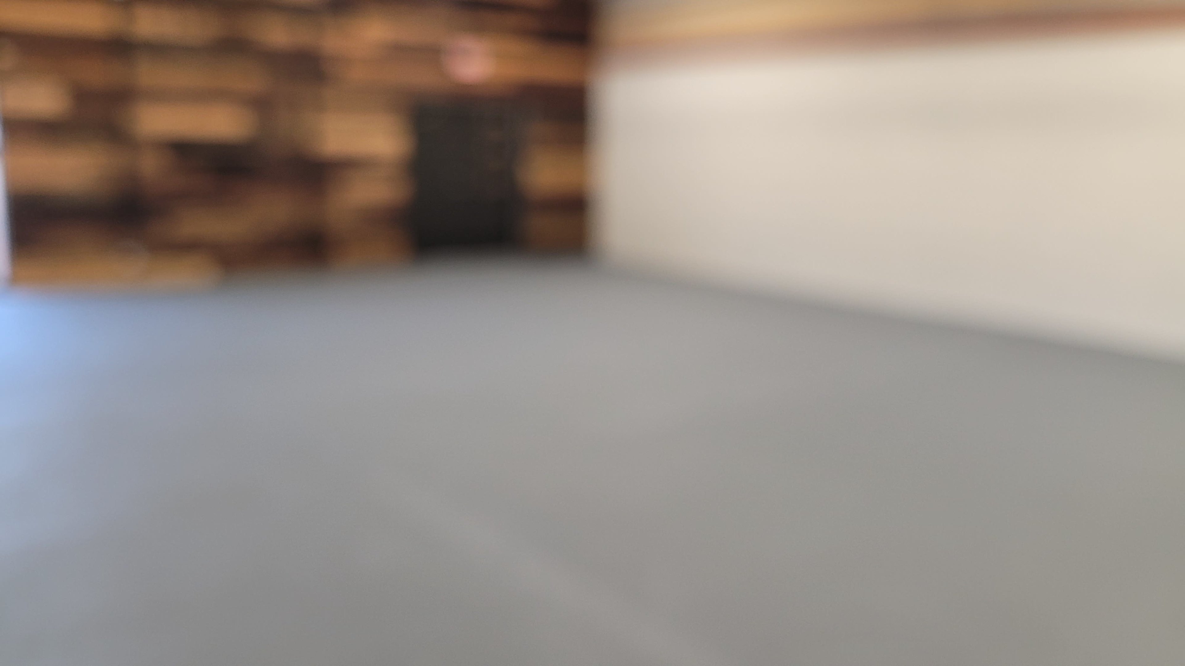 A blurred interior space with a gray floor and a wooden wall in the background.