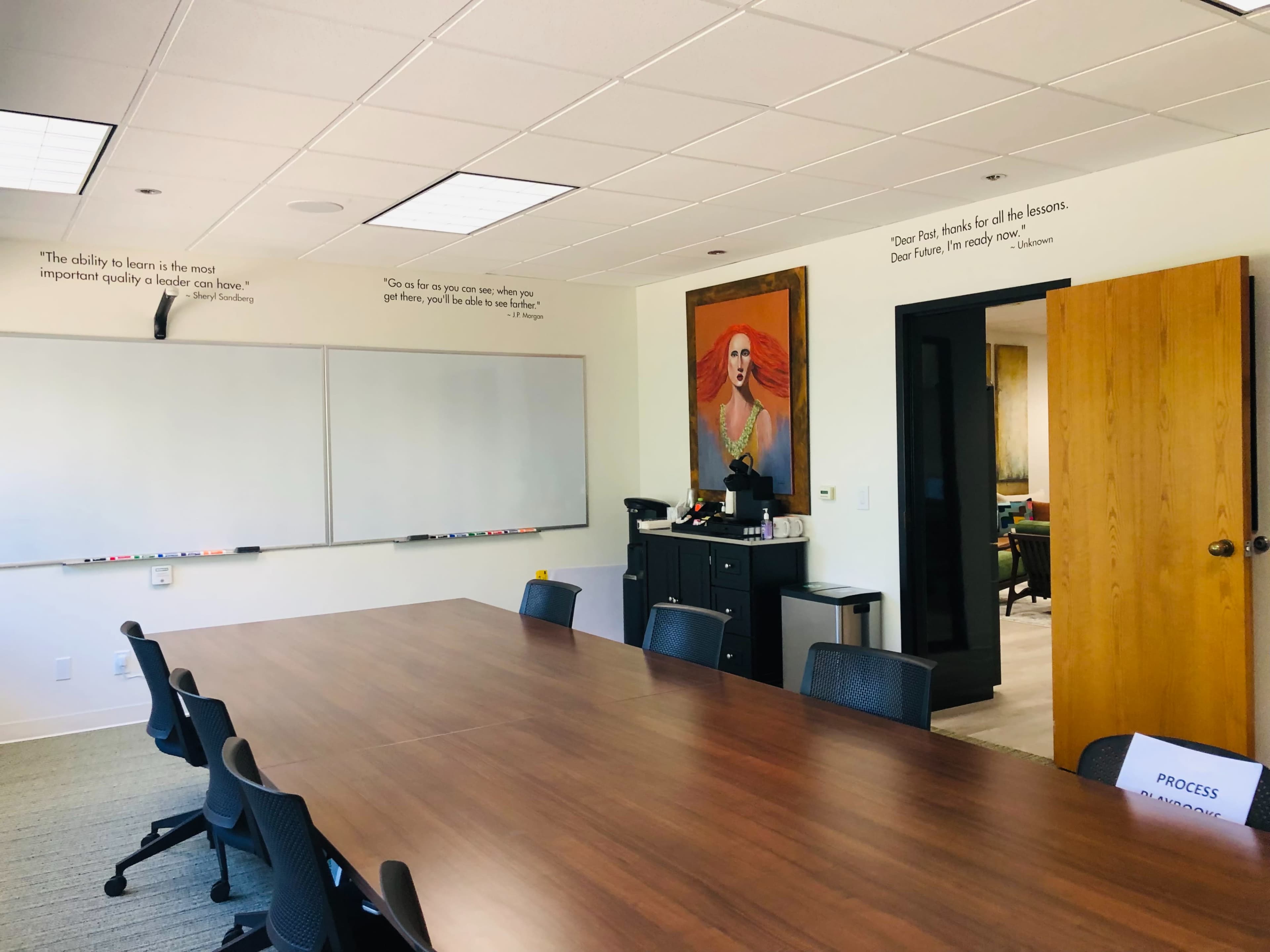 The image shows a conference room with a long wooden table, a whiteboard on the wall, and a large painting of a woman in a red dress.