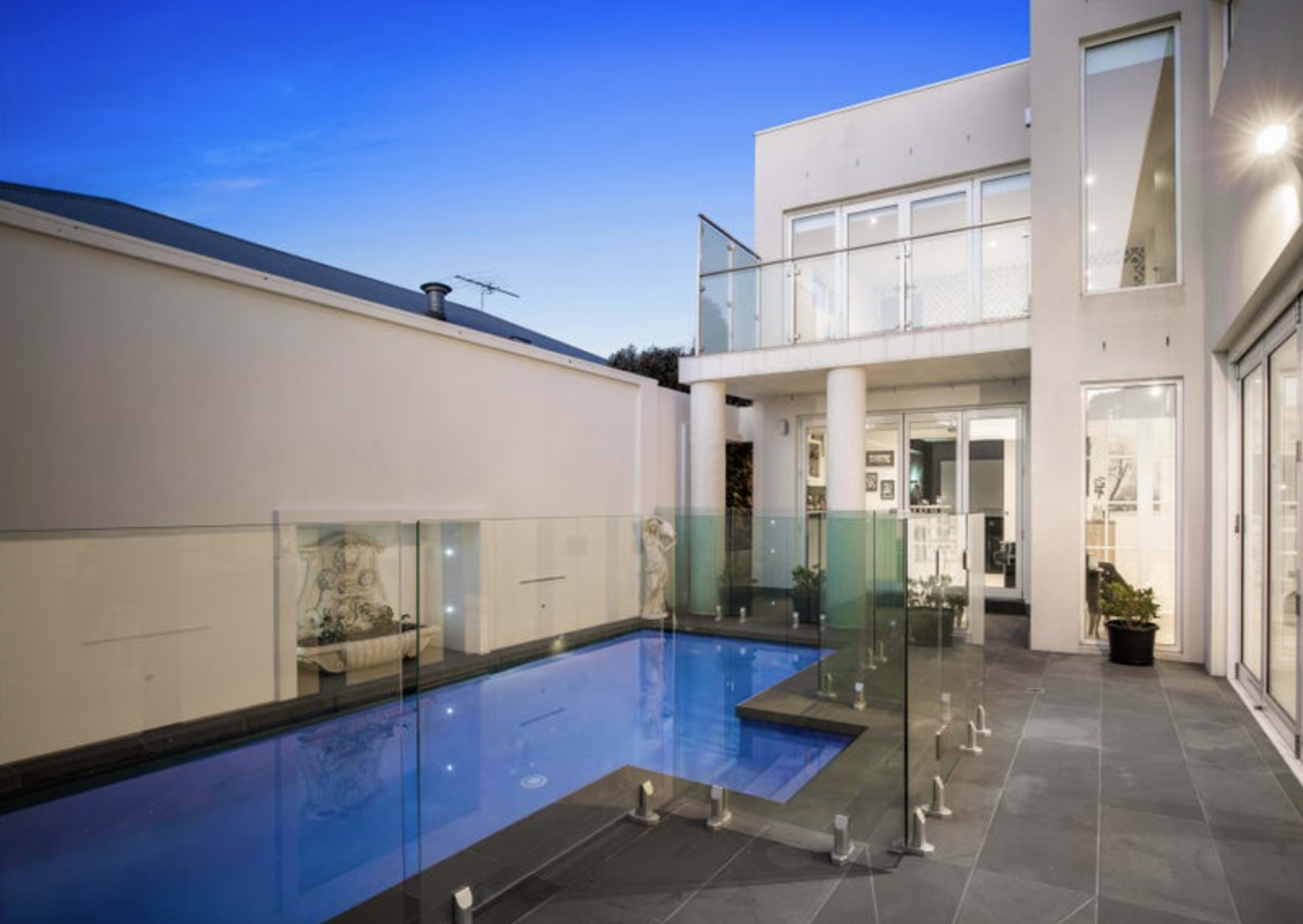 The image features a modern house with a glass-enclosed pool area and multiple large windows under a twilight sky.