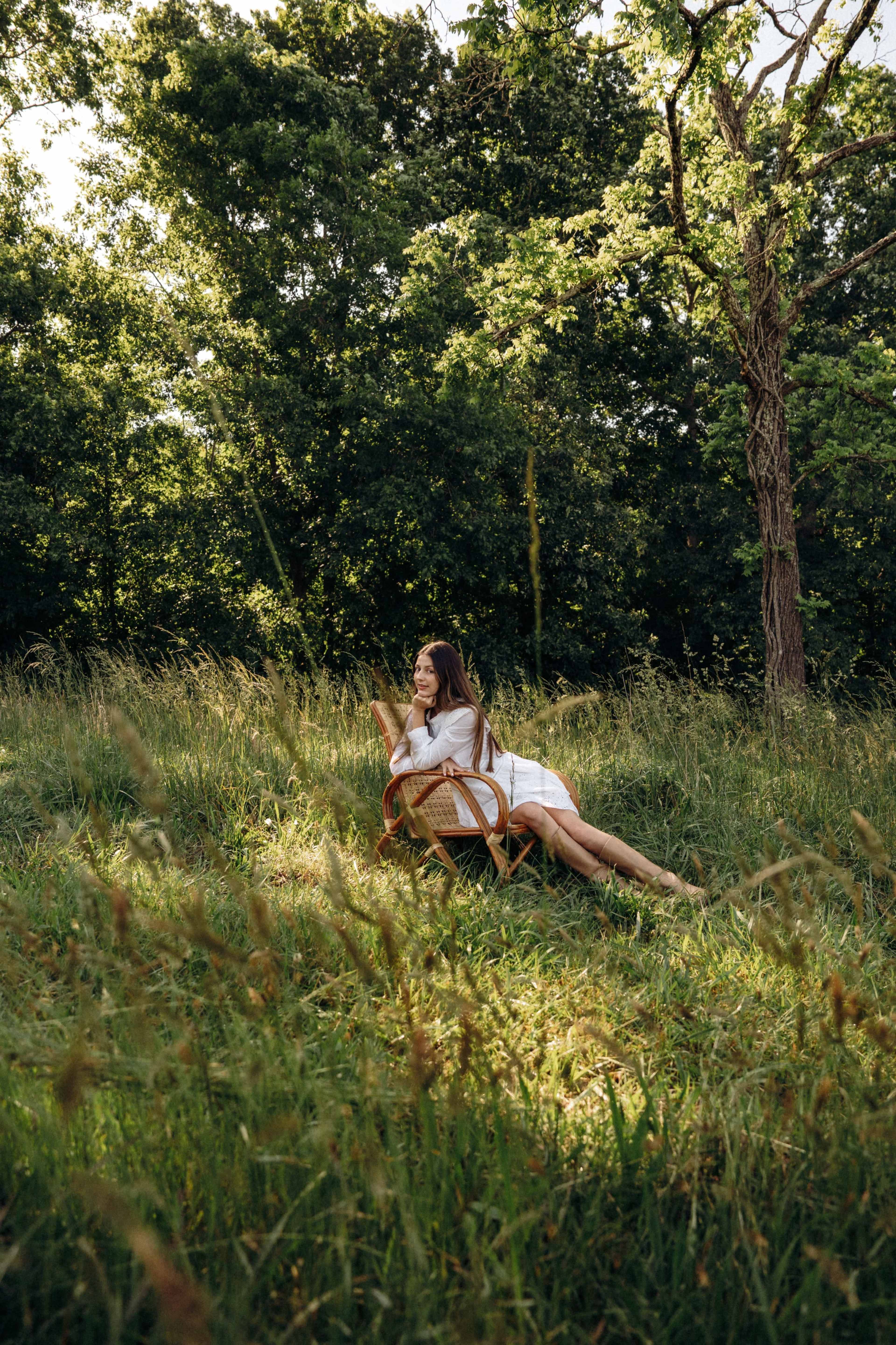 A woman is sitting on a chair in a grassy field, surrounded by trees.