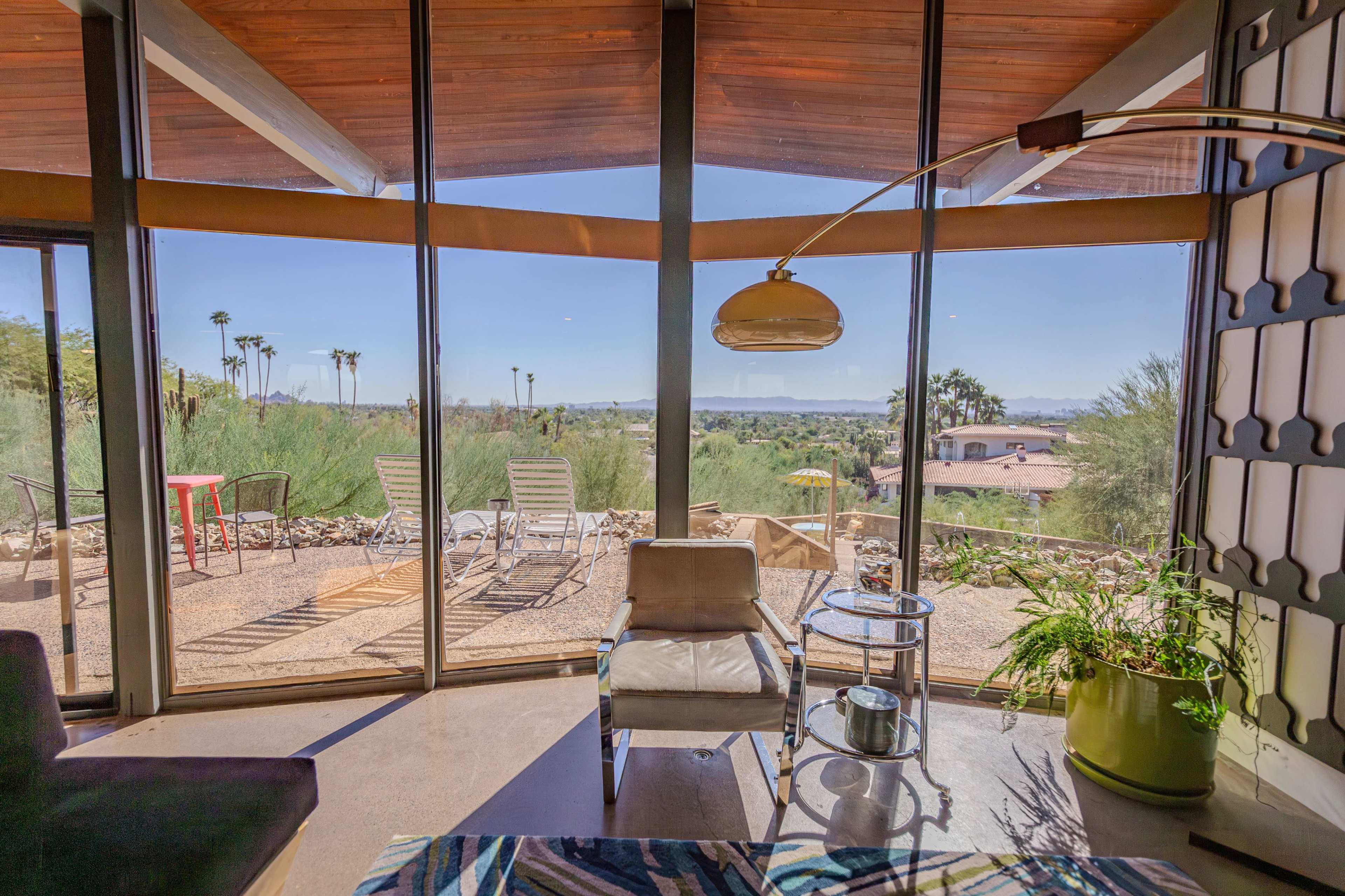 A modern sitting area with large windows overlooking a desert landscape featuring palm trees and outdoor seating.