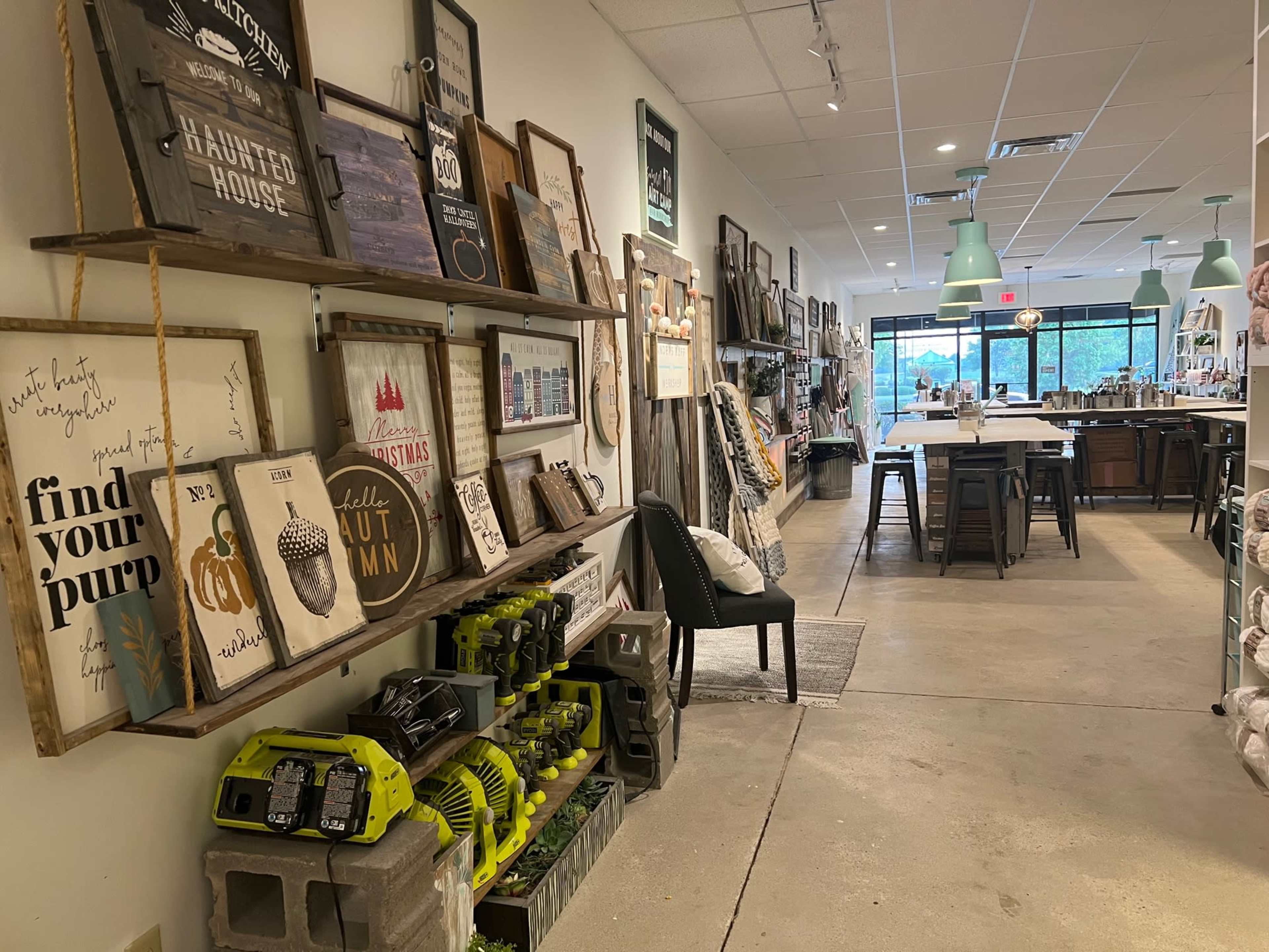 The interior of a retail store with shelves displaying various signs and home decor items, alongside a row of tools and a seating area.