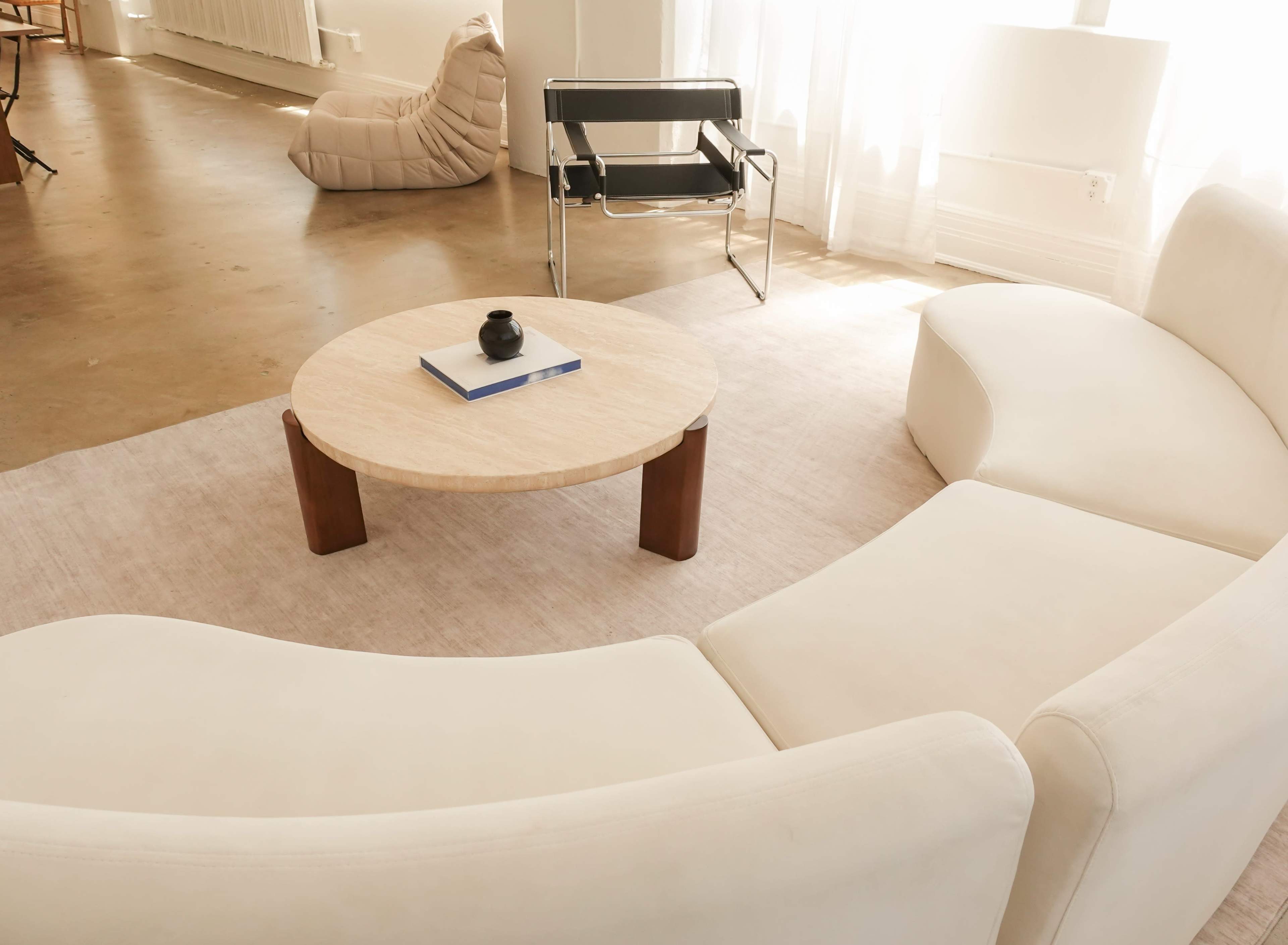 The image shows a modern living space with a curved white sofa, a round coffee table, and a black chair, all situated on a light rug.
