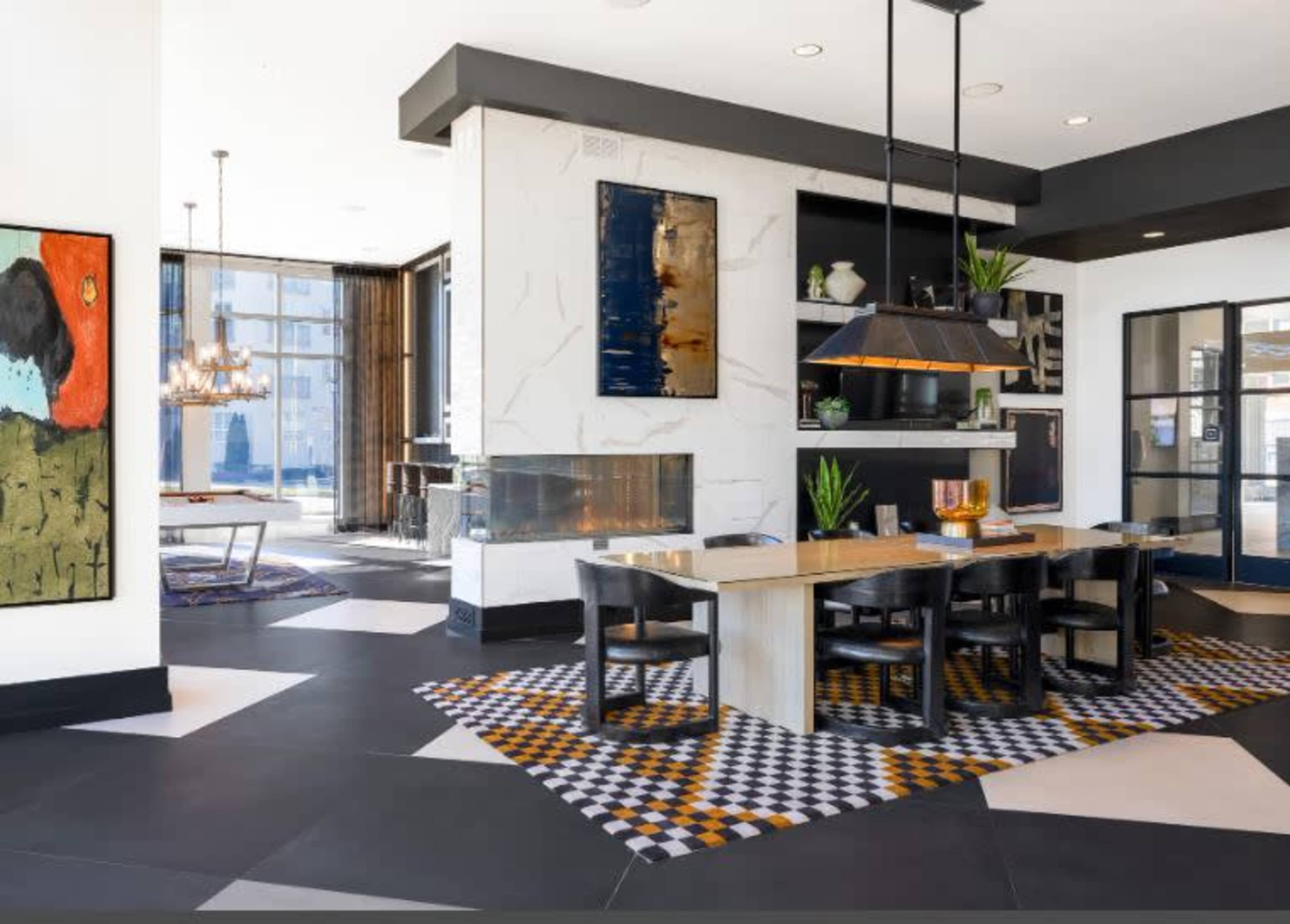The image shows a modern dining space featuring a large table, black chairs, a patterned rug, and a marble fireplace with art on the walls.