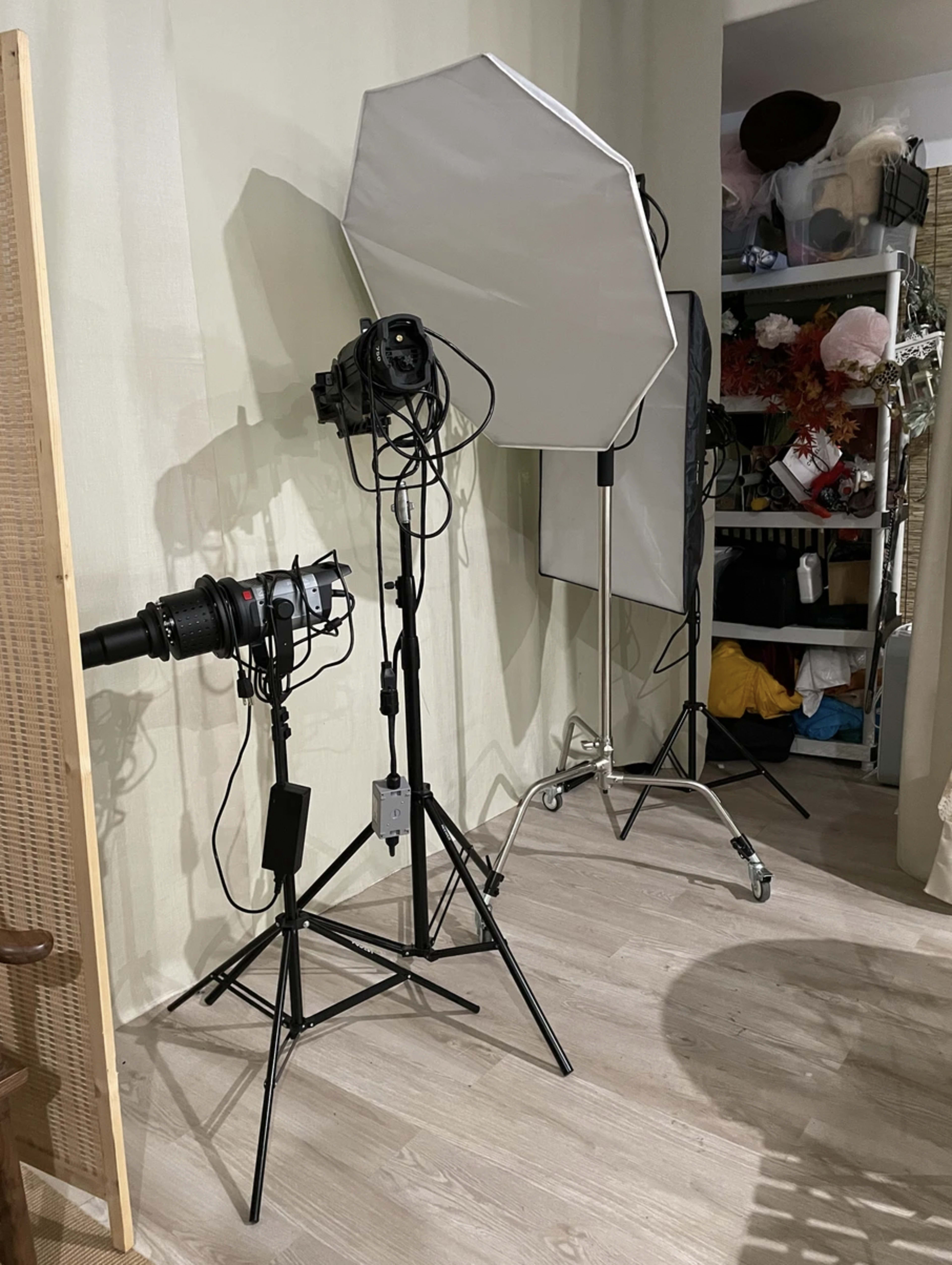 A photography setup in a room, featuring two softbox lights on tripods and a camera mounted on a tripod, with various items stored on shelves in the background.